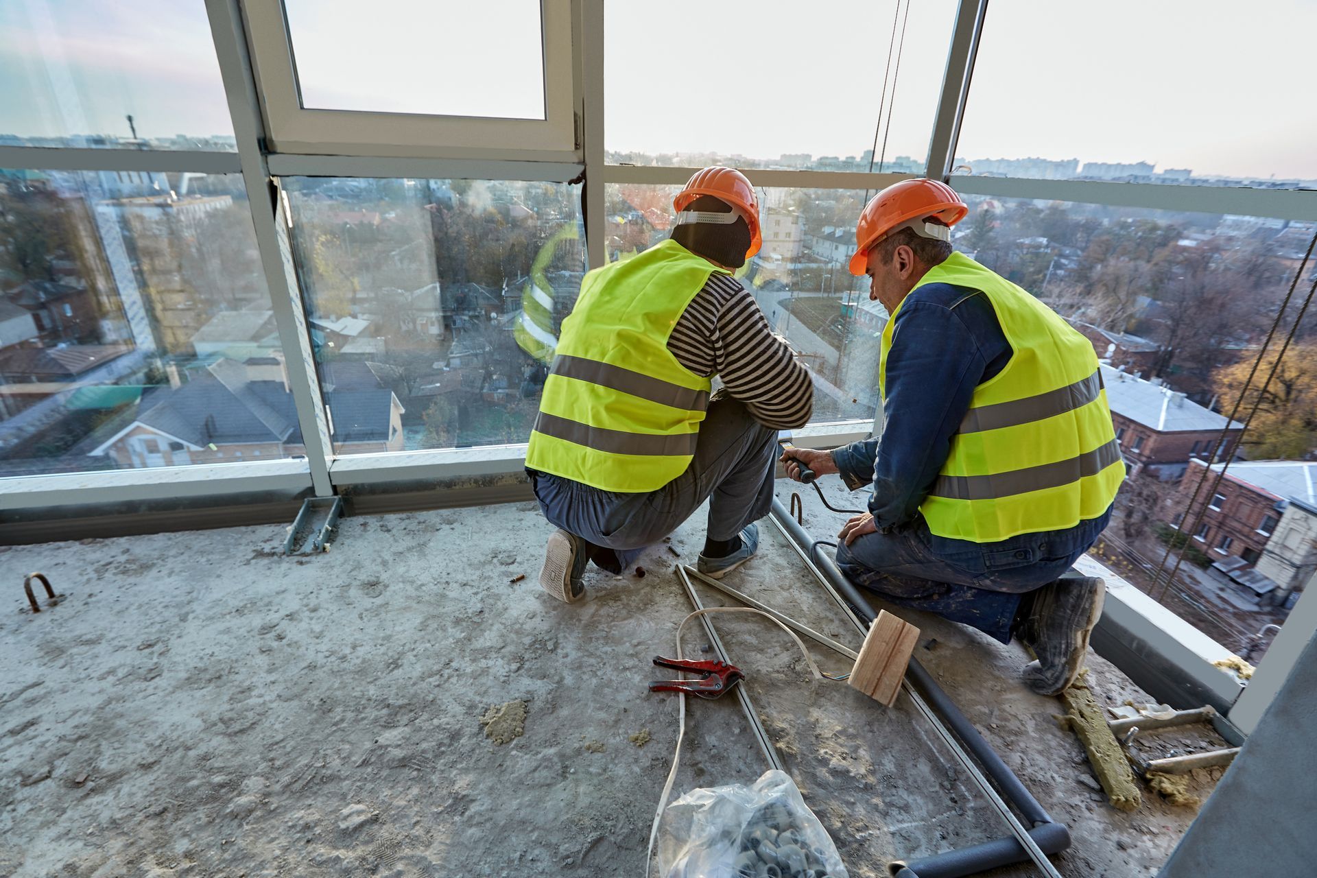 Two construction workers are working on a balcony on top of a building.