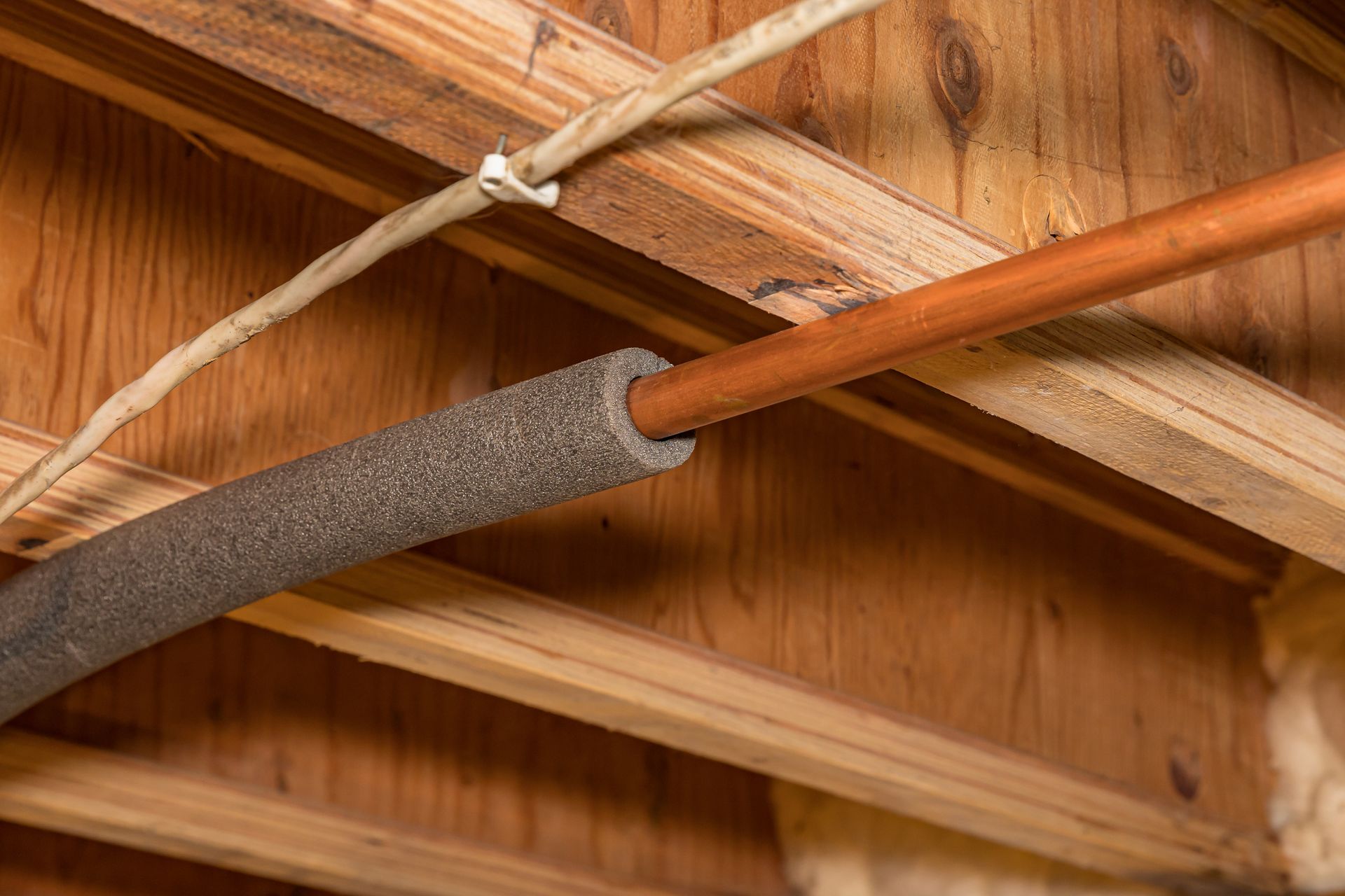A close up of a copper pipe in a wooden ceiling.