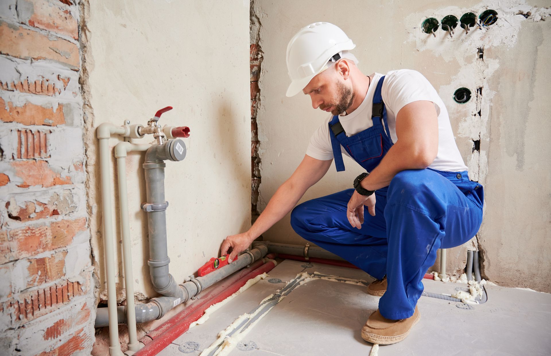 A plumber is measuring a pipe with a level in a bathroom.