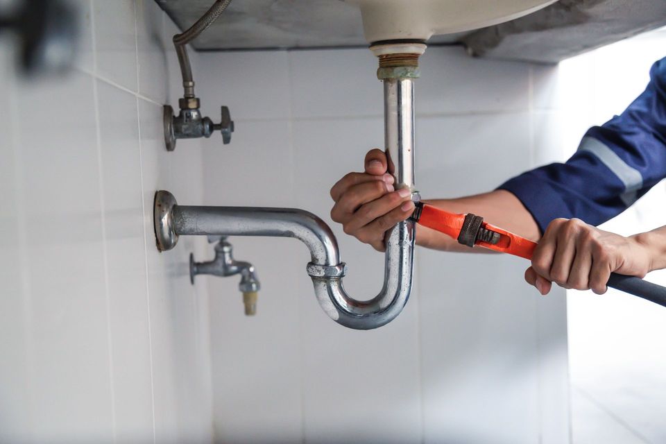 A plumber is fixing a sink pipe with a wrench.