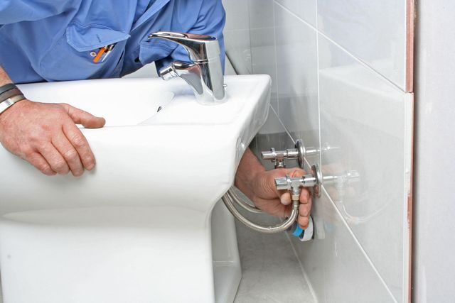A plumber is fixing a sink in a bathroom.
