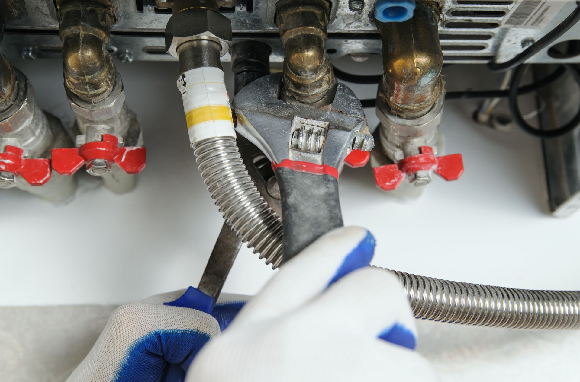 A person is working on a boiler with a wrench and pliers.