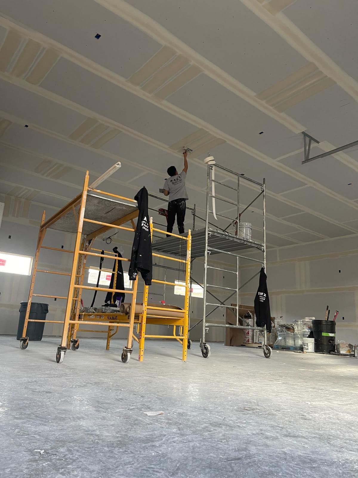 A man is painting the ceiling of a building while standing on a scaffolding.