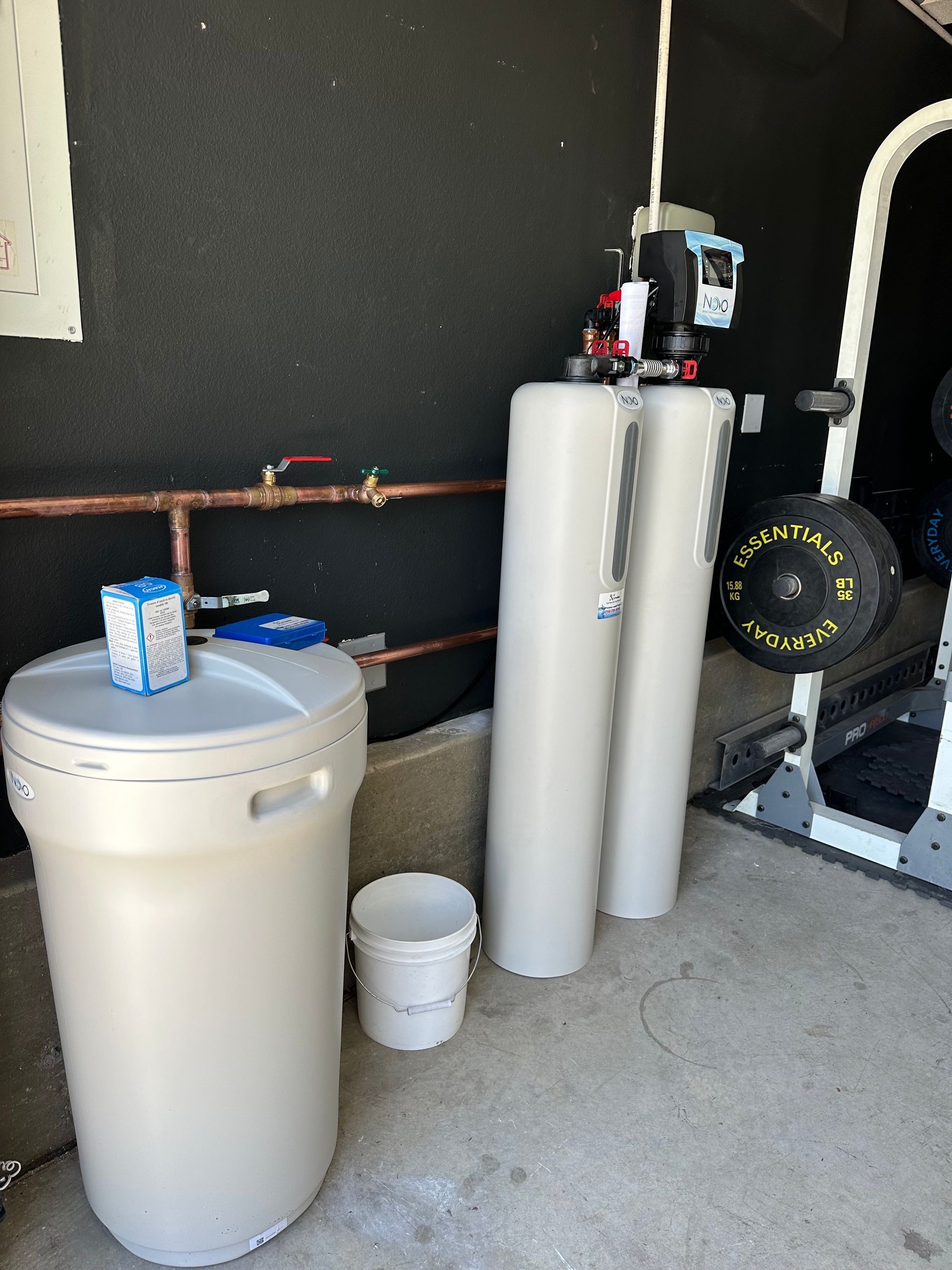 Water softener system in a garage setting, consisting of tanks, a brine tank, and copper piping.