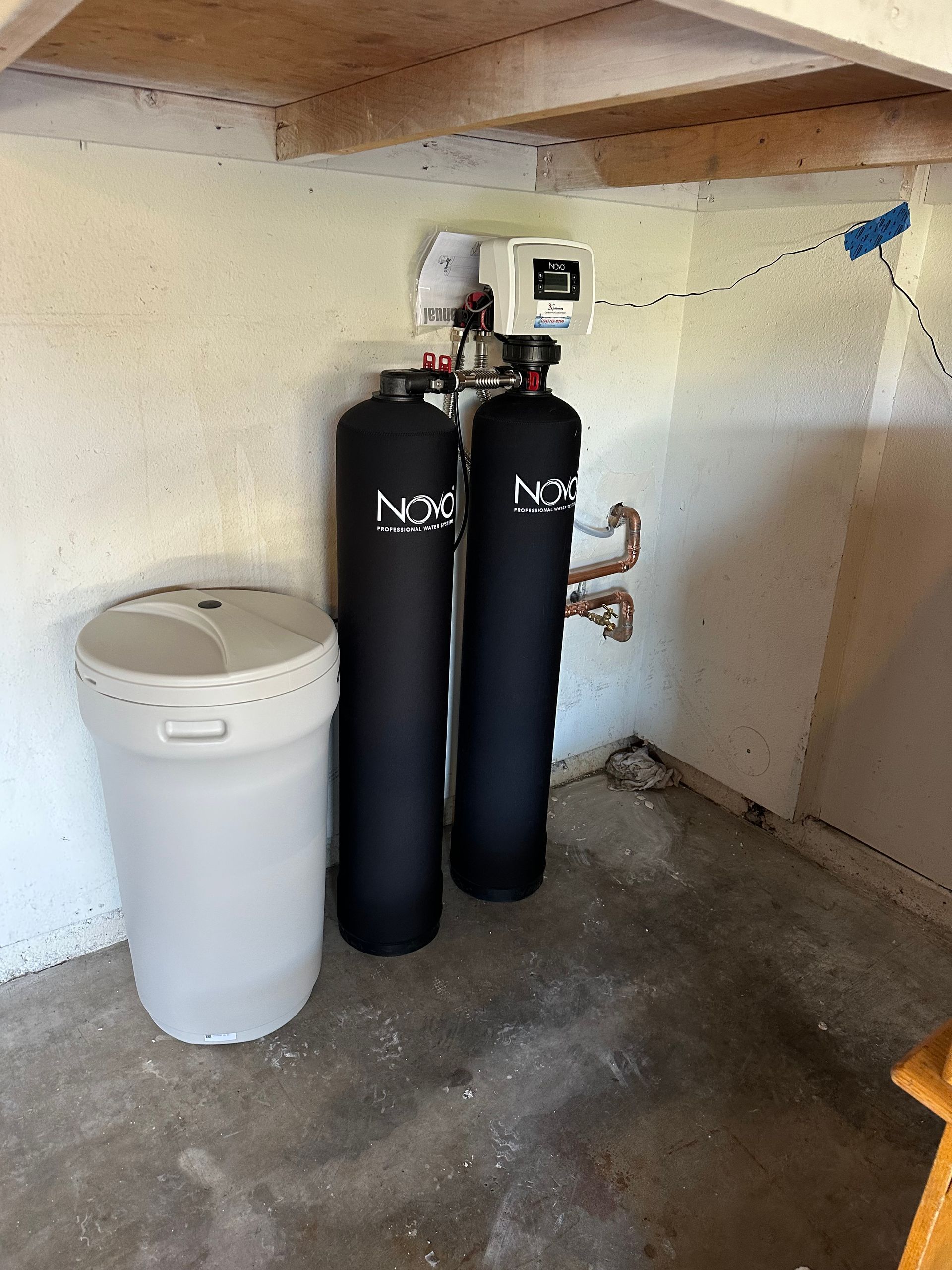 Water softener system in a basement corner.  Two black tanks, a white salt tank, and control panel.