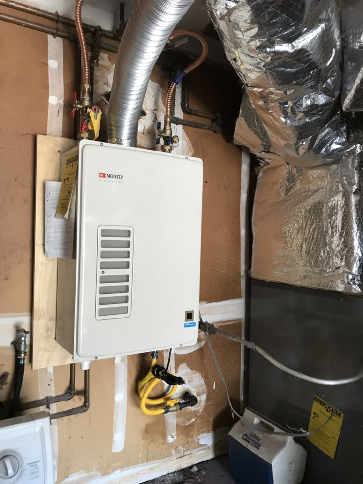 A white water heater is hanging on a wall in a room.