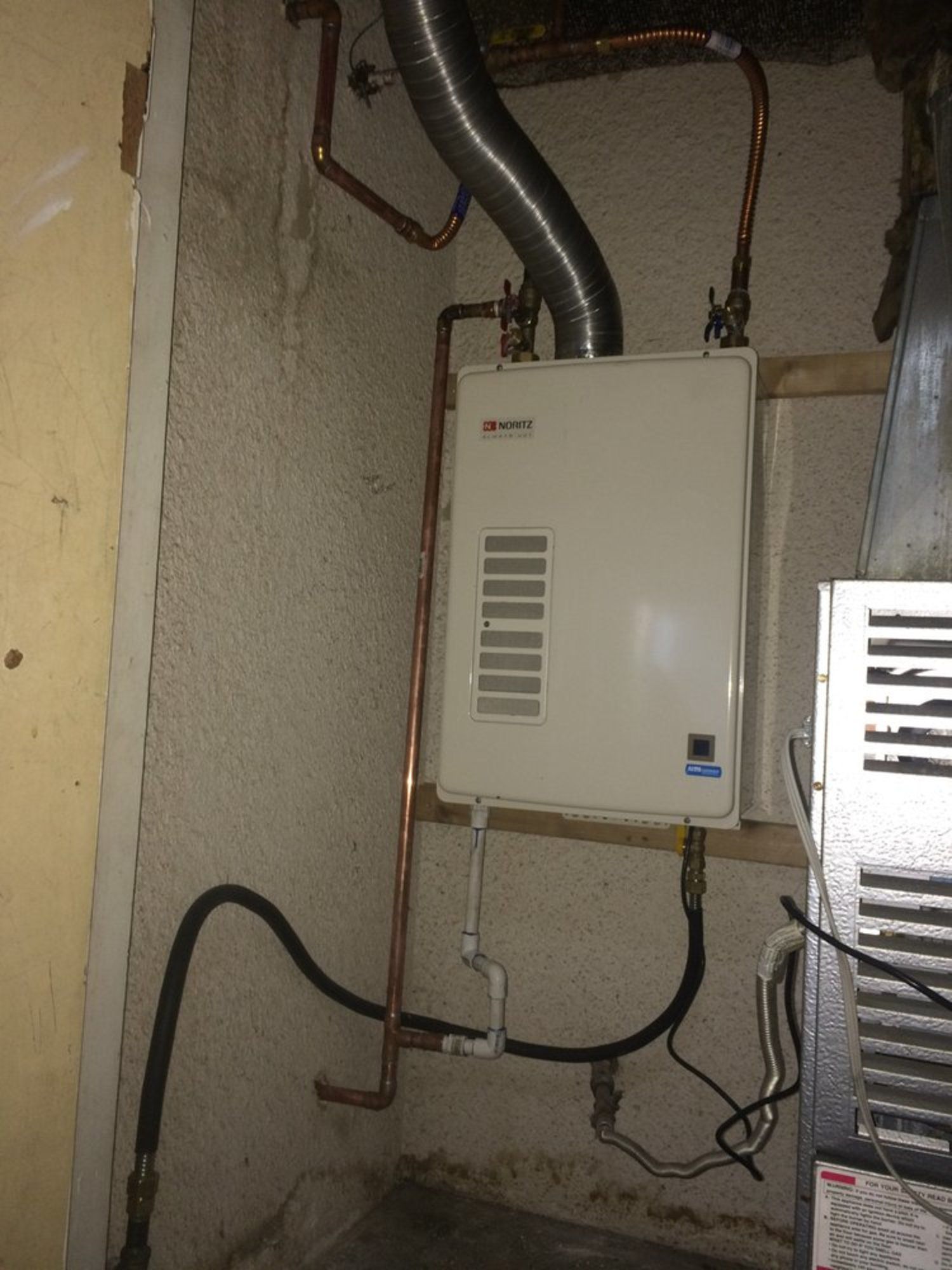 A white water heater is attached to a wall in a room.