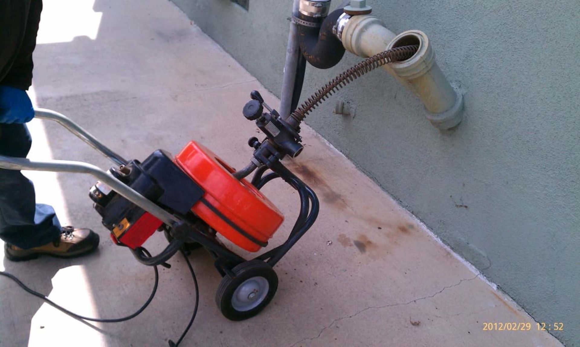A man is using a drain cleaner on a sidewalk