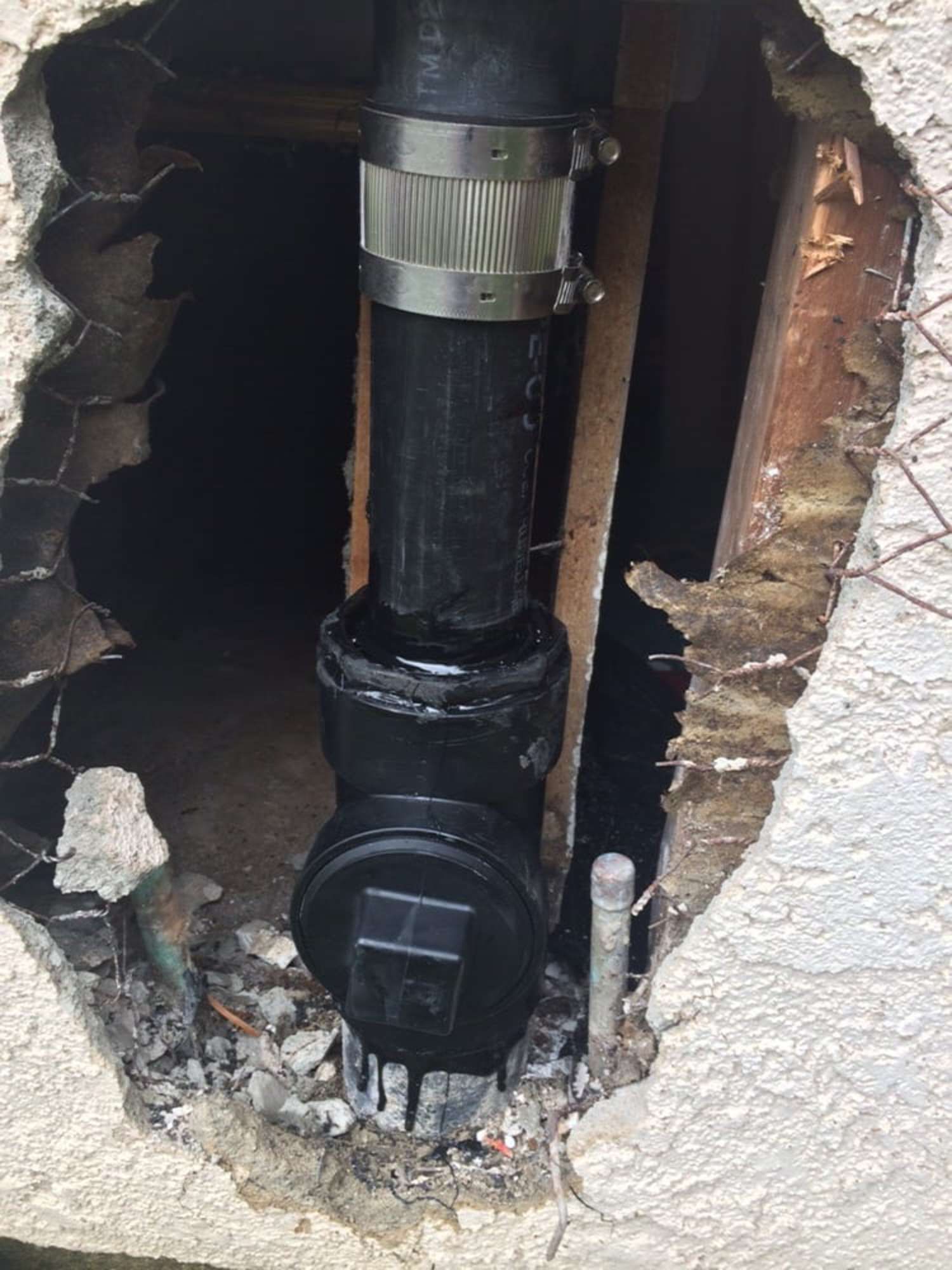 A black pipe is coming out of a hole in a wall.
