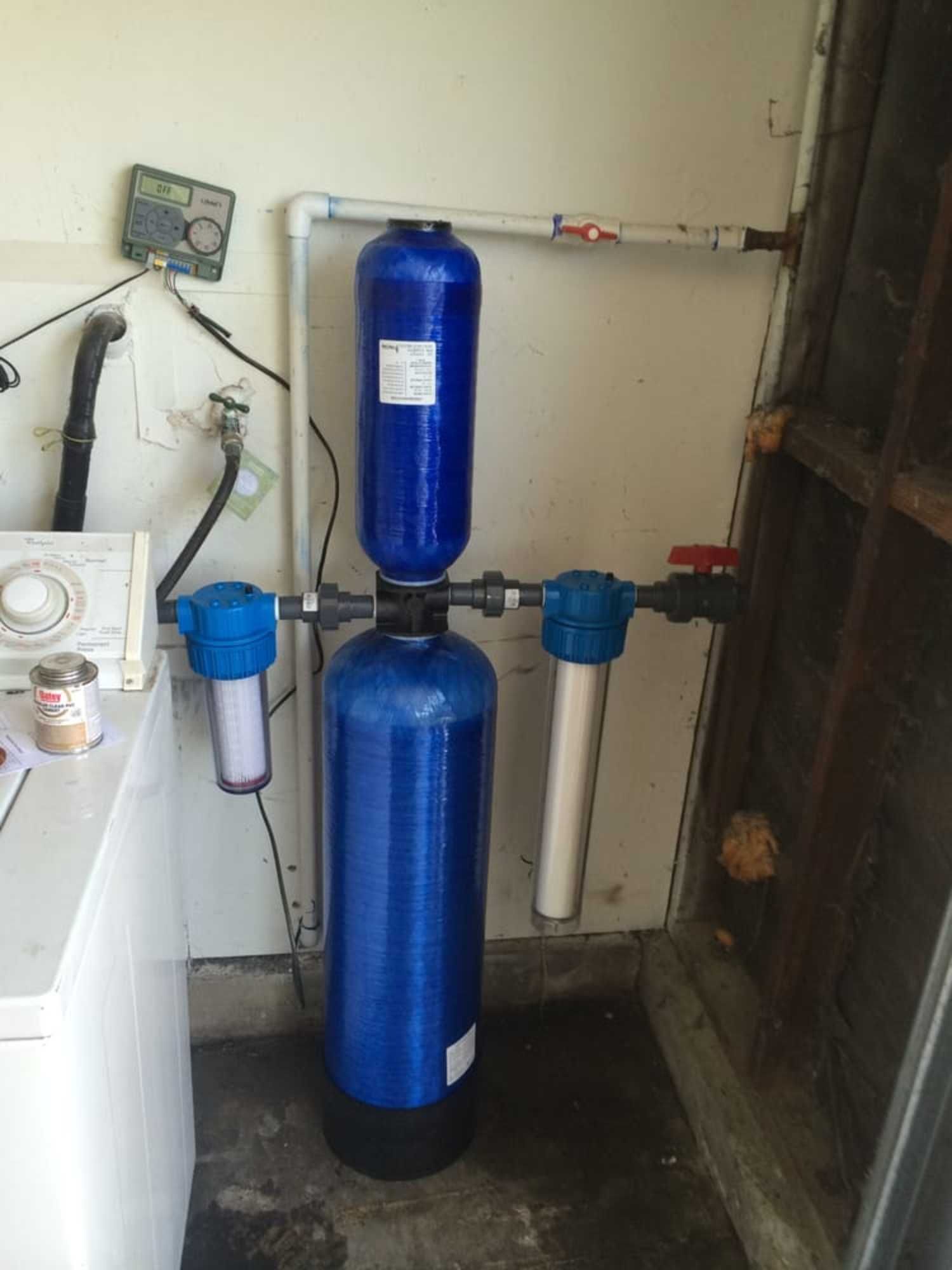 A blue water filter is sitting in a laundry room next to a washer and dryer.