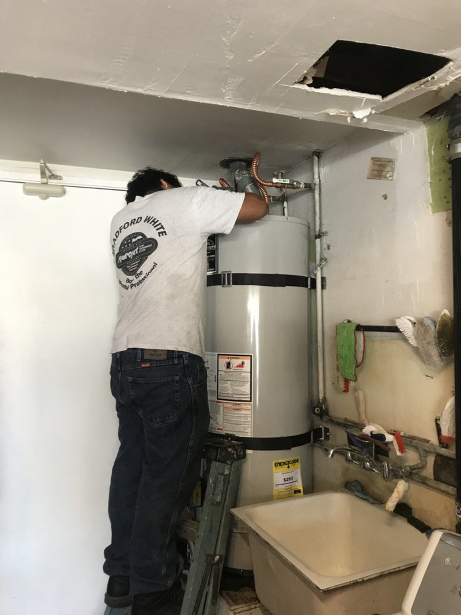 A man is standing on a ladder fixing a water heater.