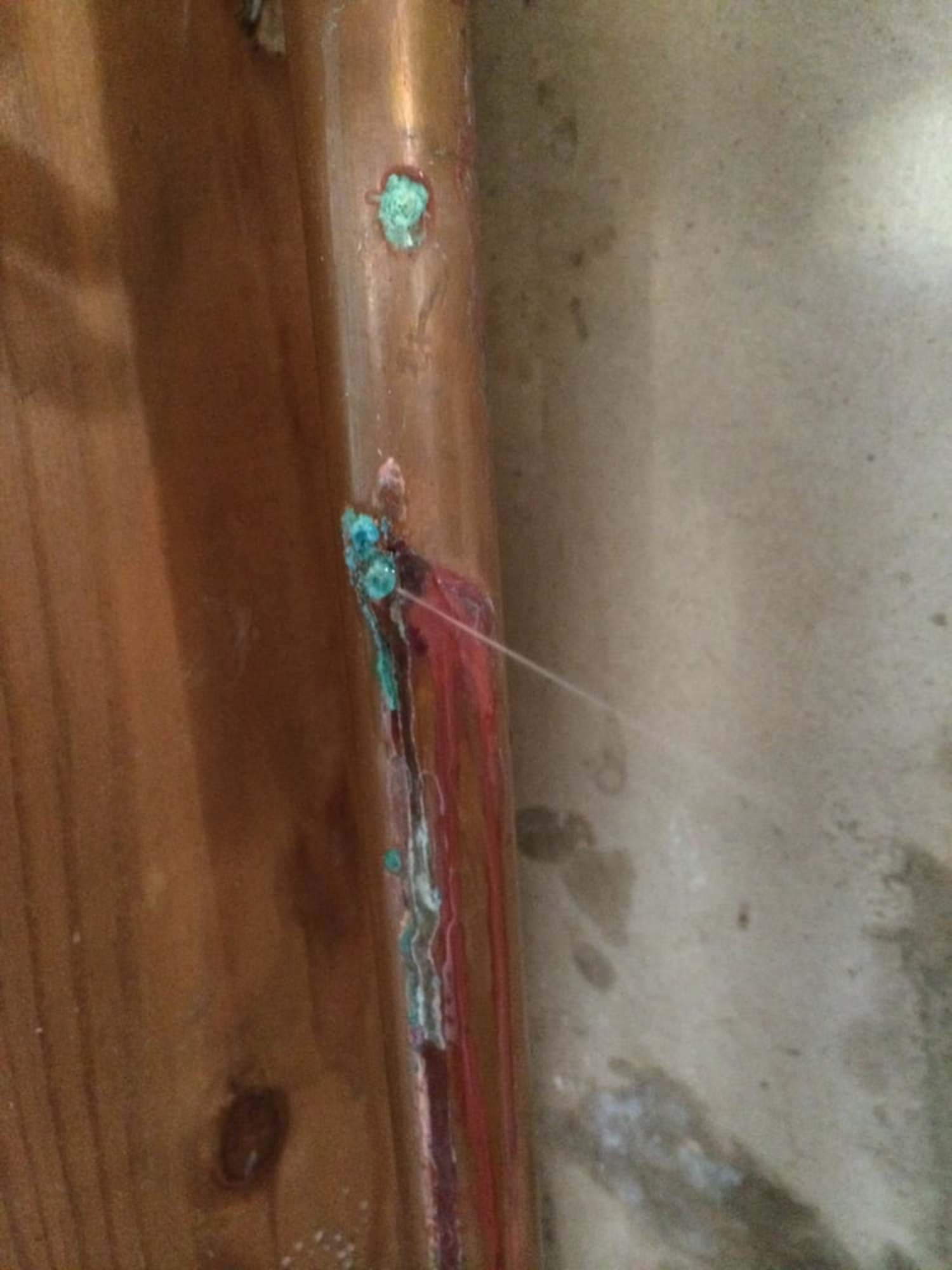 A close up of a copper pipe against a wooden wall.