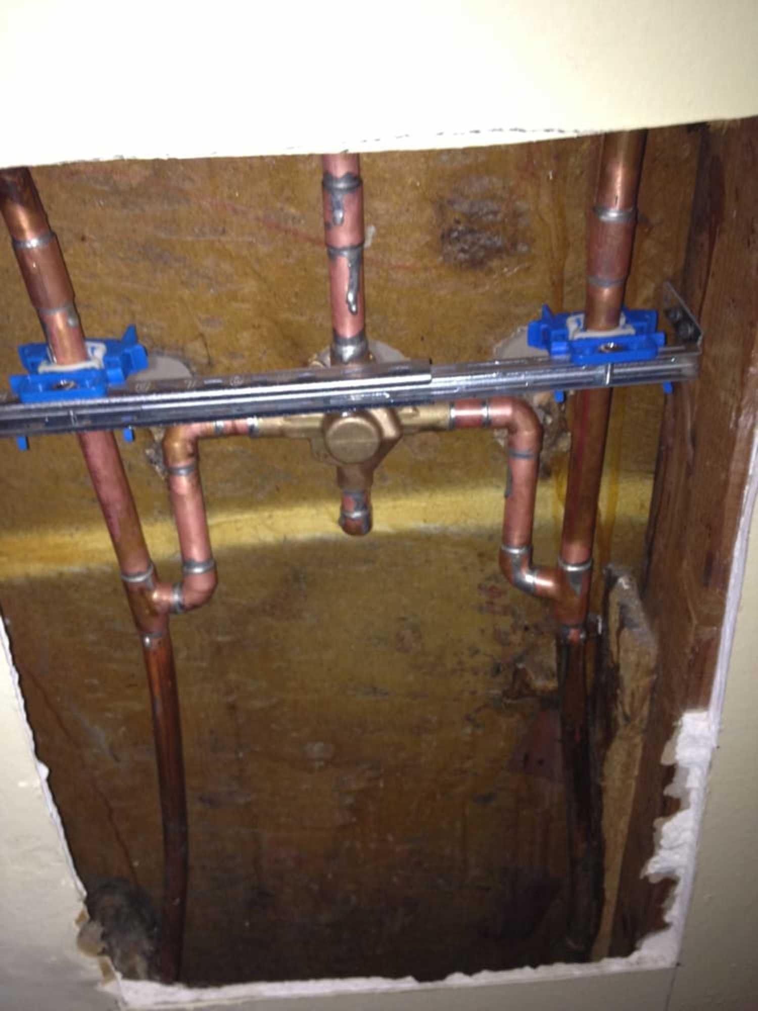 A bunch of copper pipes are coming out of a hole in the wall.