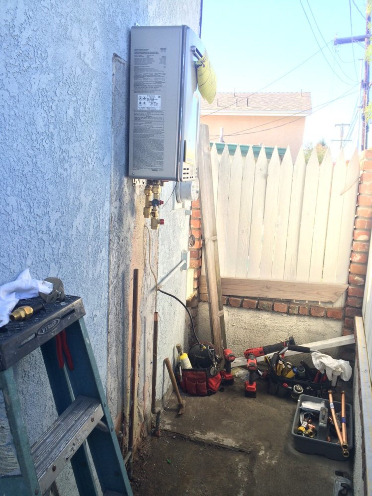 A ladder is sitting next to a water heater on the side of a building.