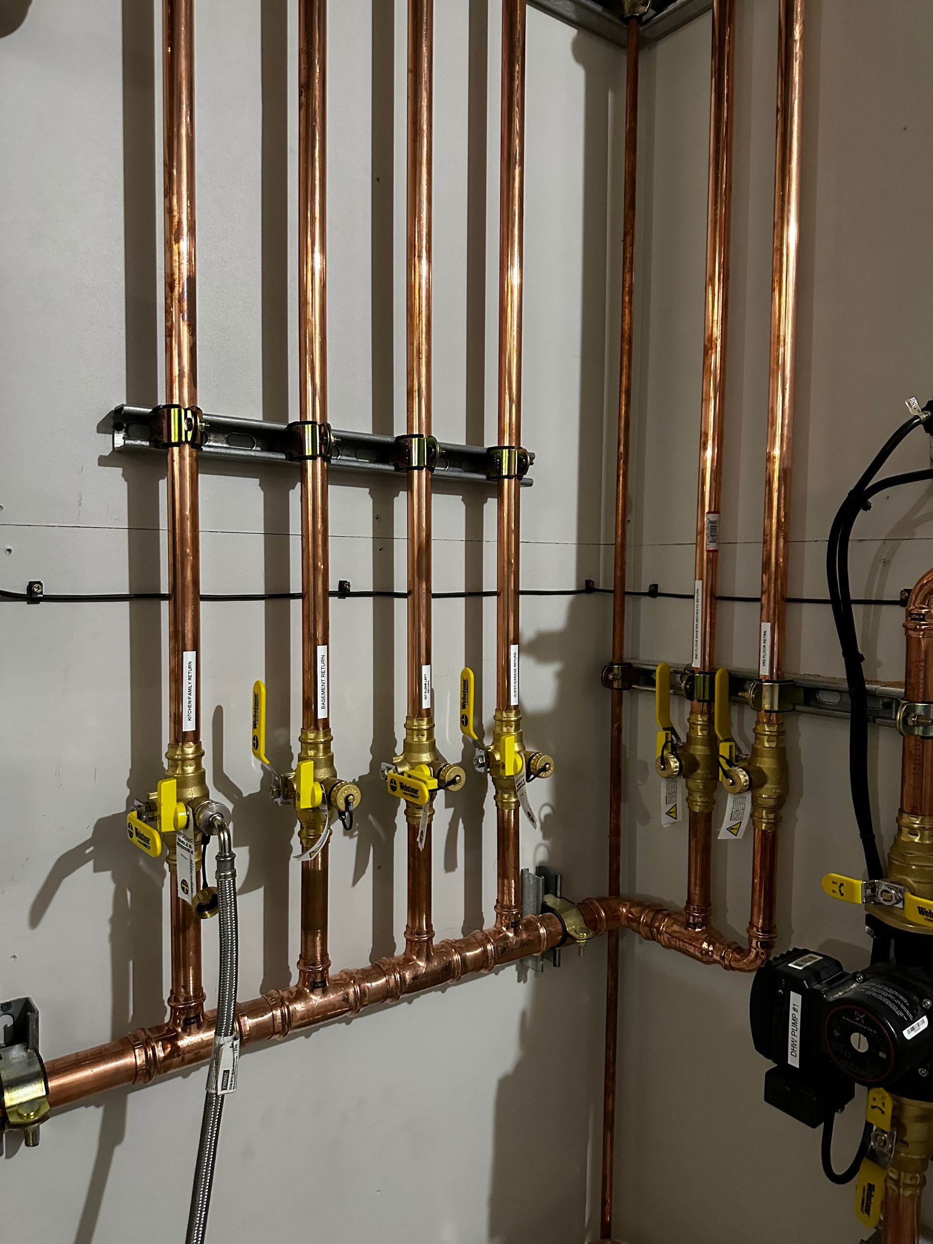 Copper piping system with valves and manifold mounted on a wall, showing residential plumbing infrastructure.