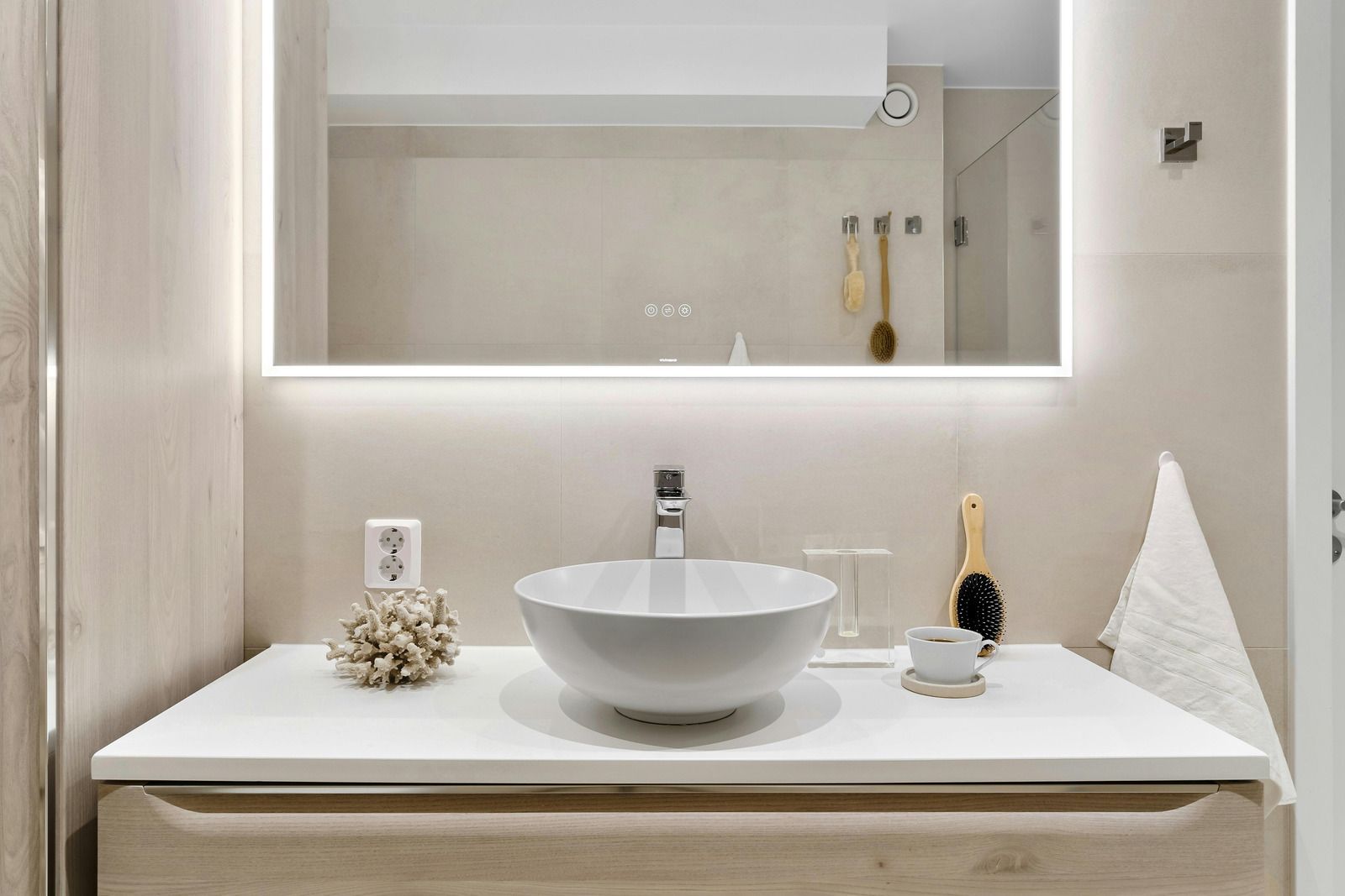 Modern bathroom vanity with a white vessel sink, wooden cabinet, and backlit rectangular mirror on a light beige wall.