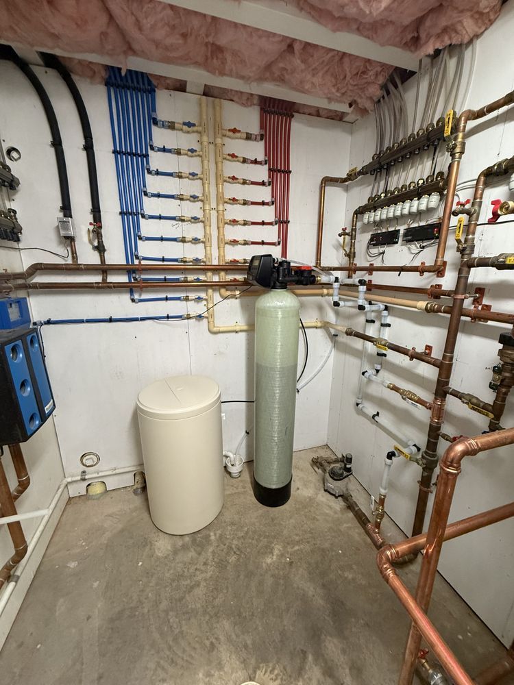 Utility room featuring residential water treatment equipment, copper piping, and a blue-and-red PEX manifold wall.