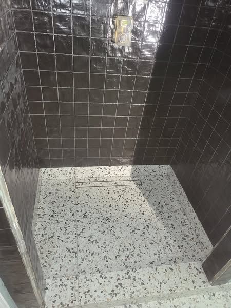 A walk in shower with black tiles and a white floor.
