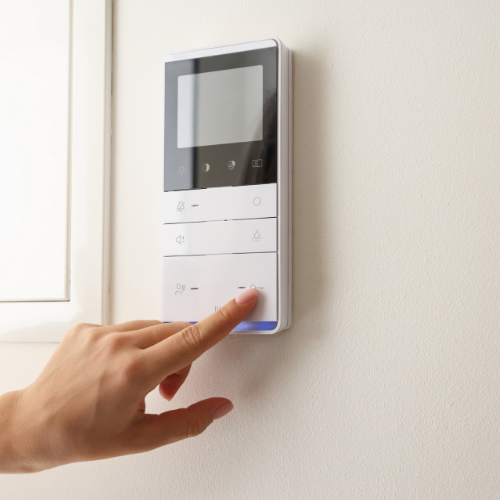 A hand presses a button on a white, wall-mounted digital control panel with a black display screen.