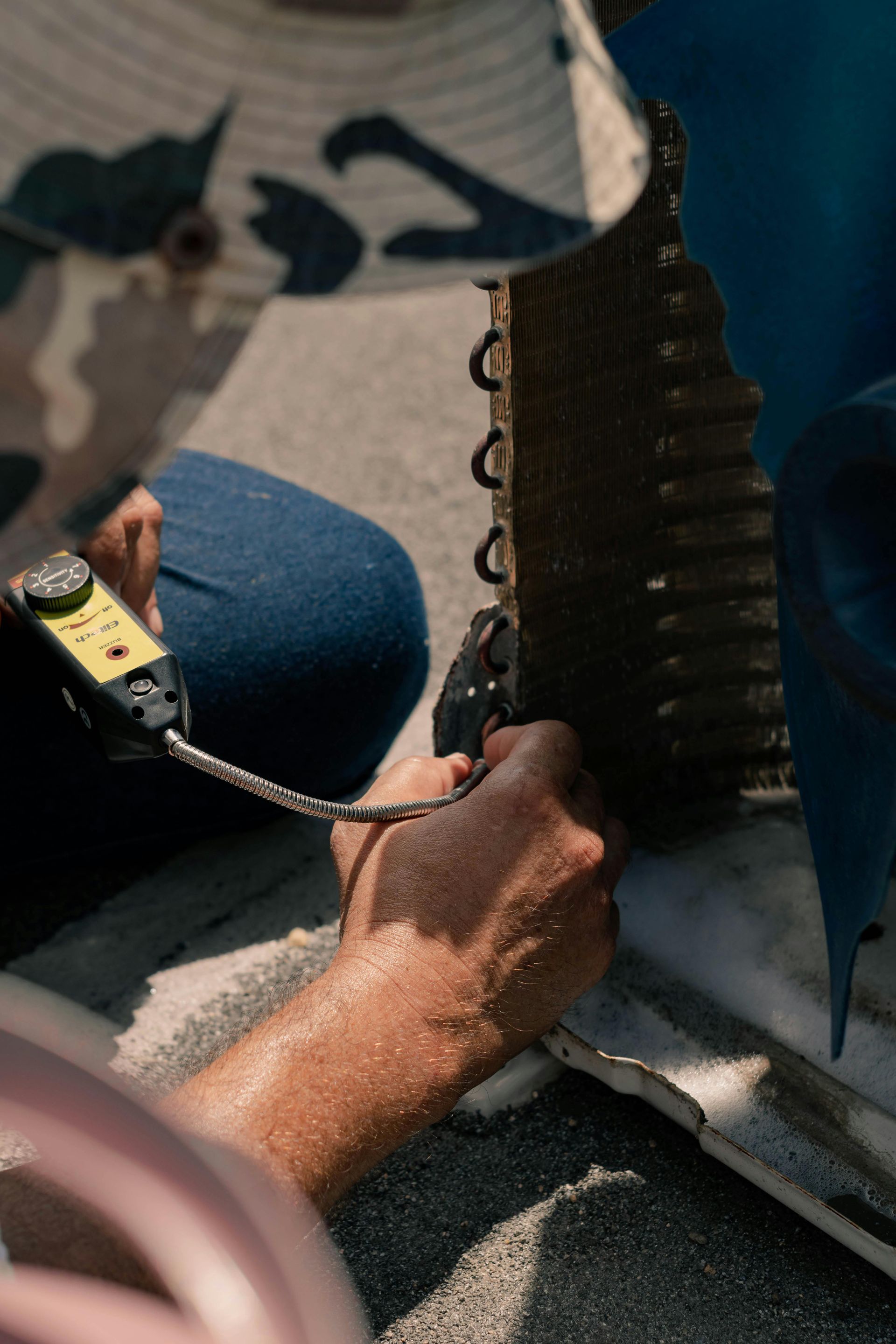 A person uses a handheld diagnostic tool to test the metal fins of an outdoor air conditioning unit.