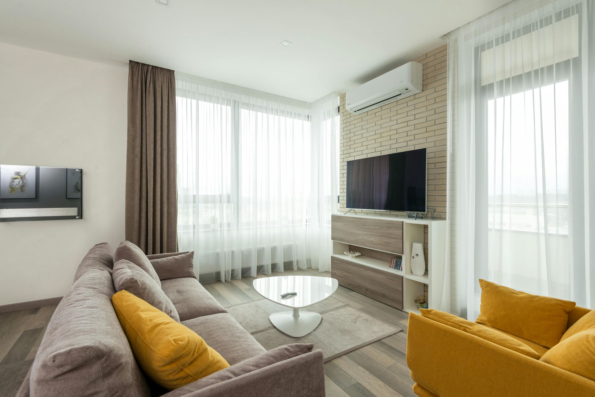 A modern living room with a grey sofa featuring mustard yellow pillows, a matching armchair, and a TV on a wood unit.