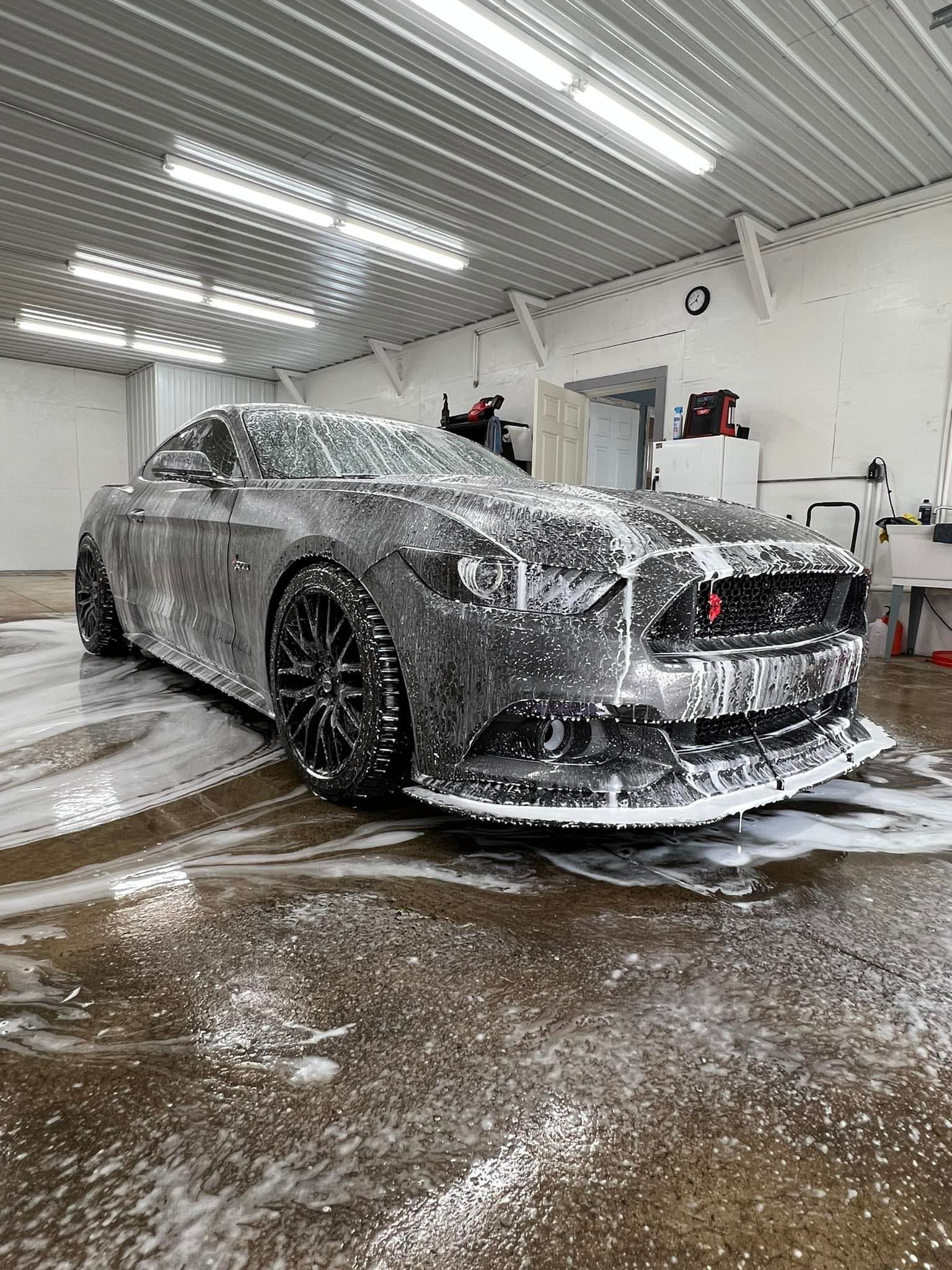 Black Ford Mustang covered in soapy foam inside a garage.