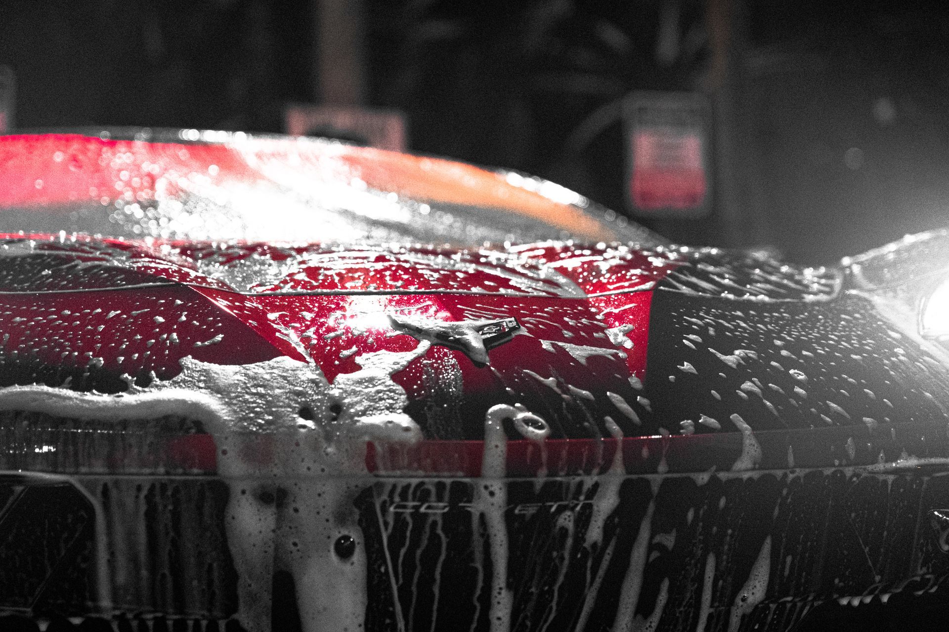 Red car being washed, covered in soap suds, headlight illuminated.