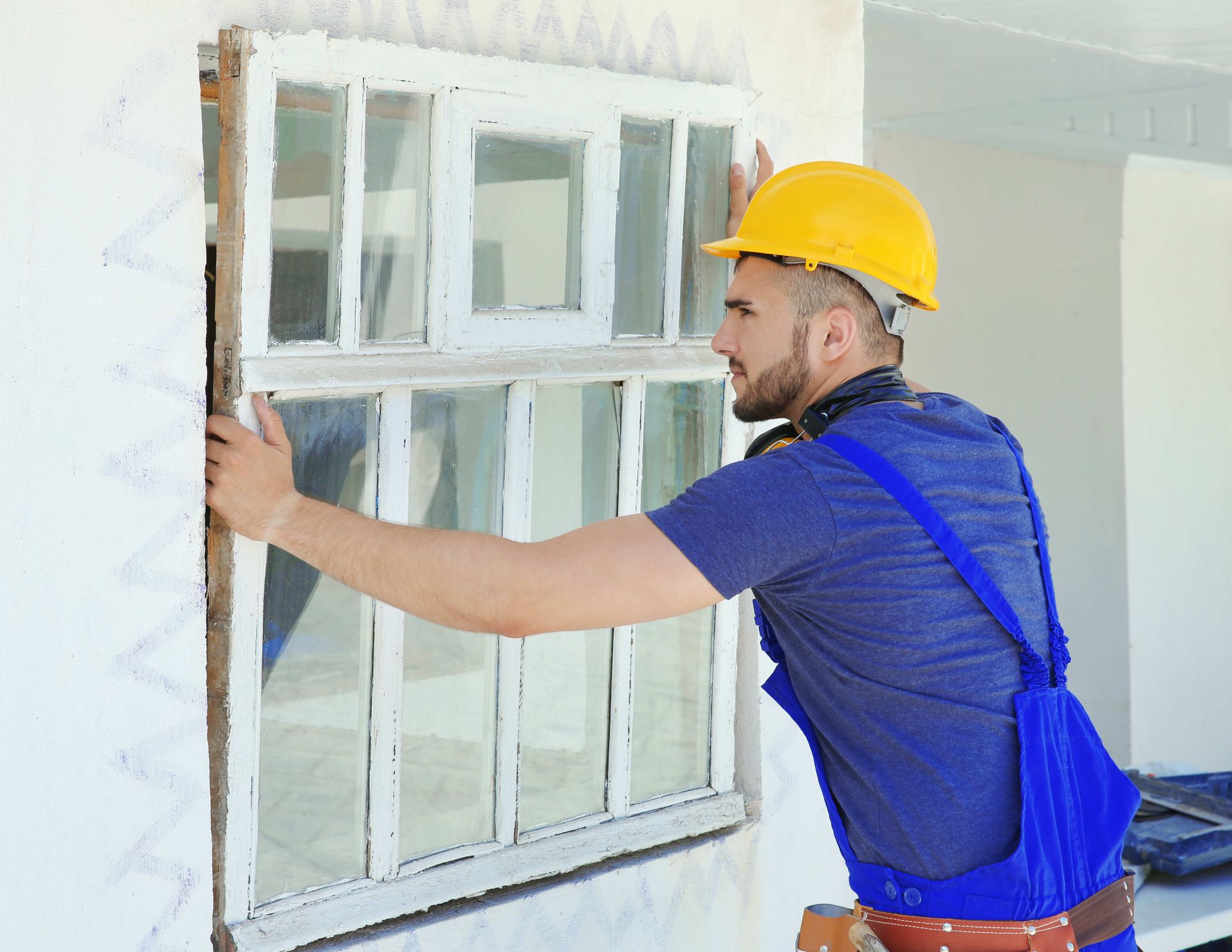 A man in a hard hat is installing a window on a wall.