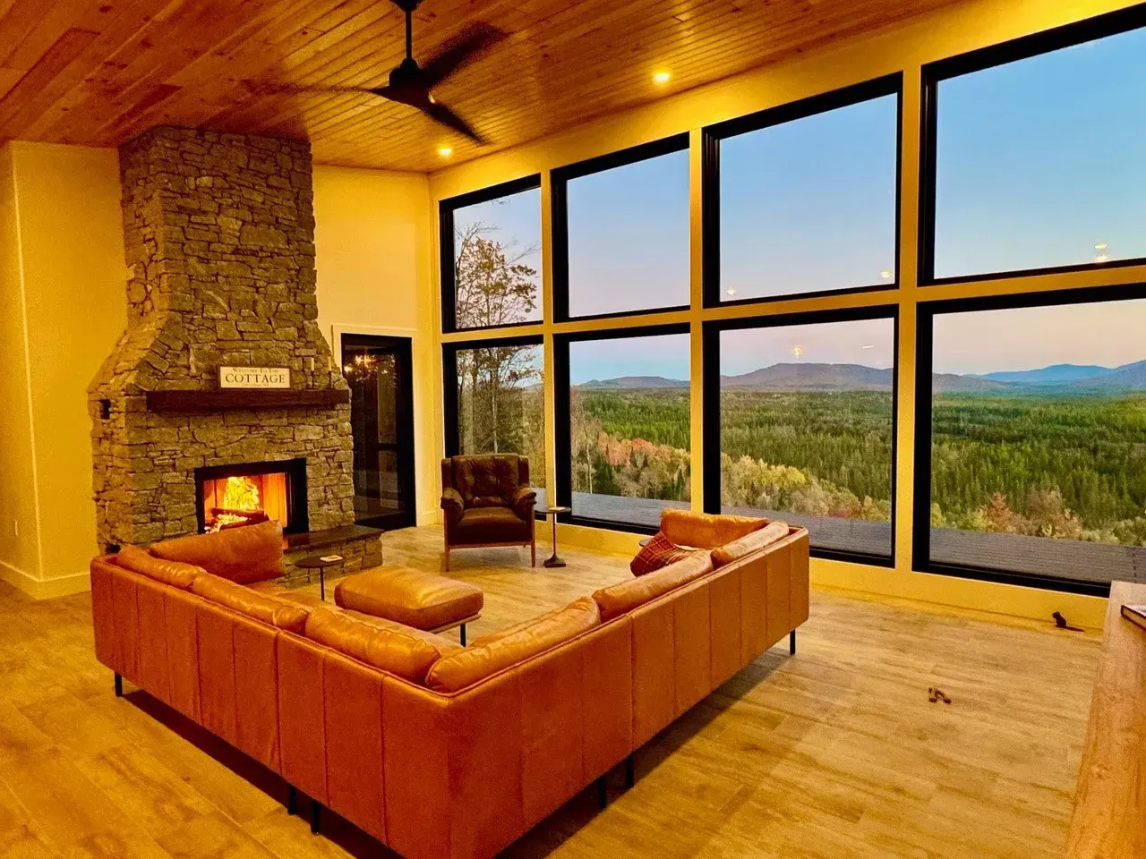 Living room with a stone fireplace, leather sectional sofa, and large windows overlooking a scenic vista.