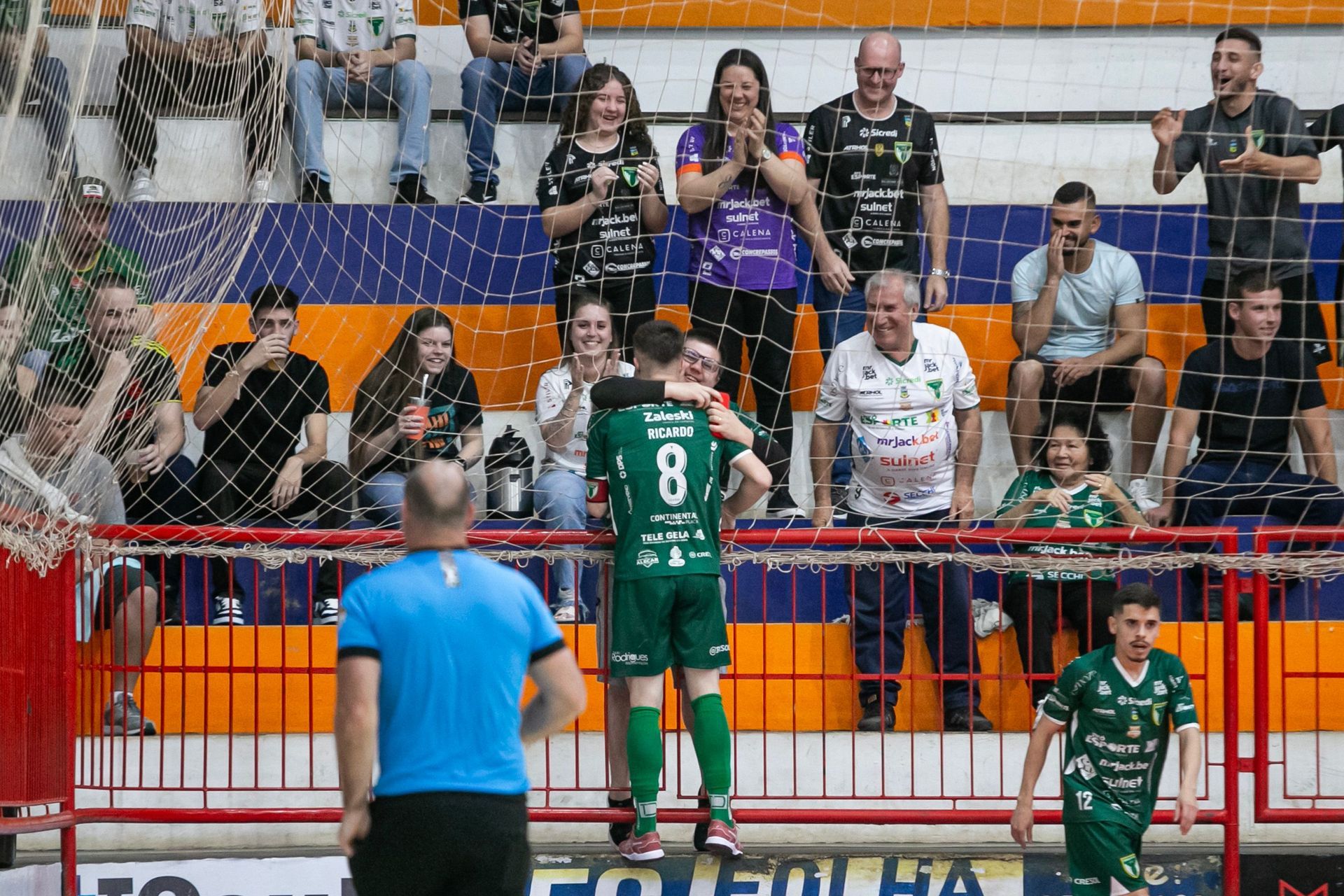 Jogador abraçando e comemorando com torcedor no ginásio.