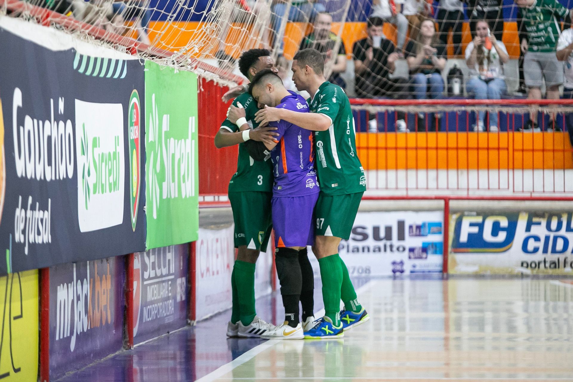 Um grupo de jogadores de futebol se abraçam na quadra