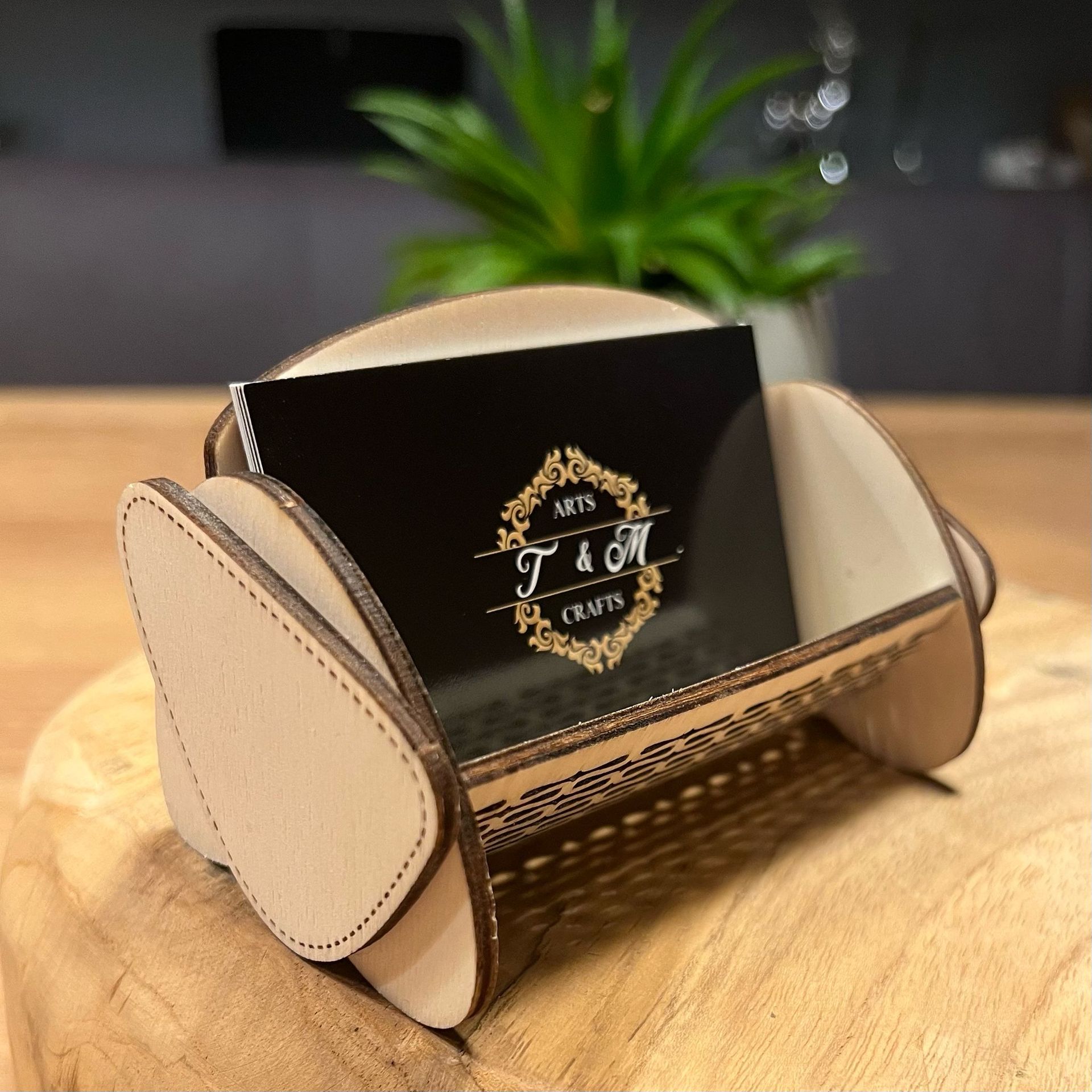 Ein Holzschild von T & M Crafts steht auf einem Tisch neben einer Pflanze.