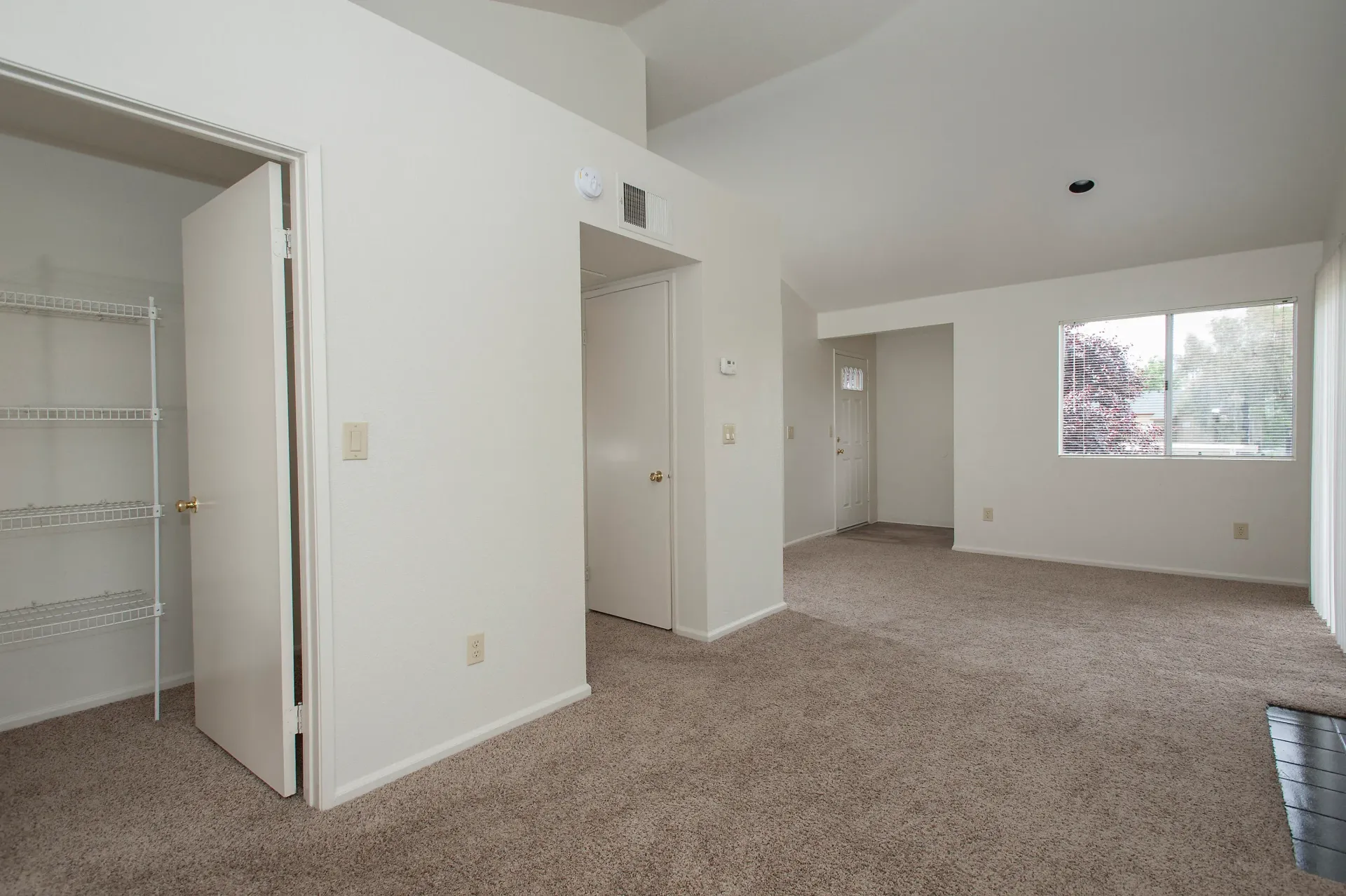 Interior living area with beige carpet, a closet with wire shelving, and a window.