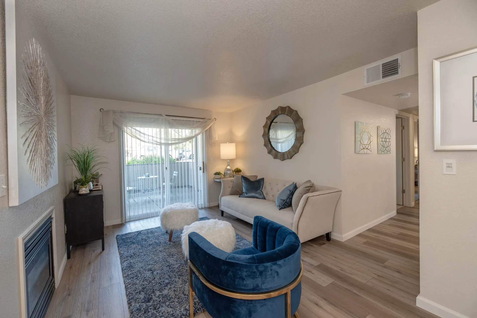 Living room with light sofa, blue velvet accent chair, rug, and sliding glass door to the balcony.