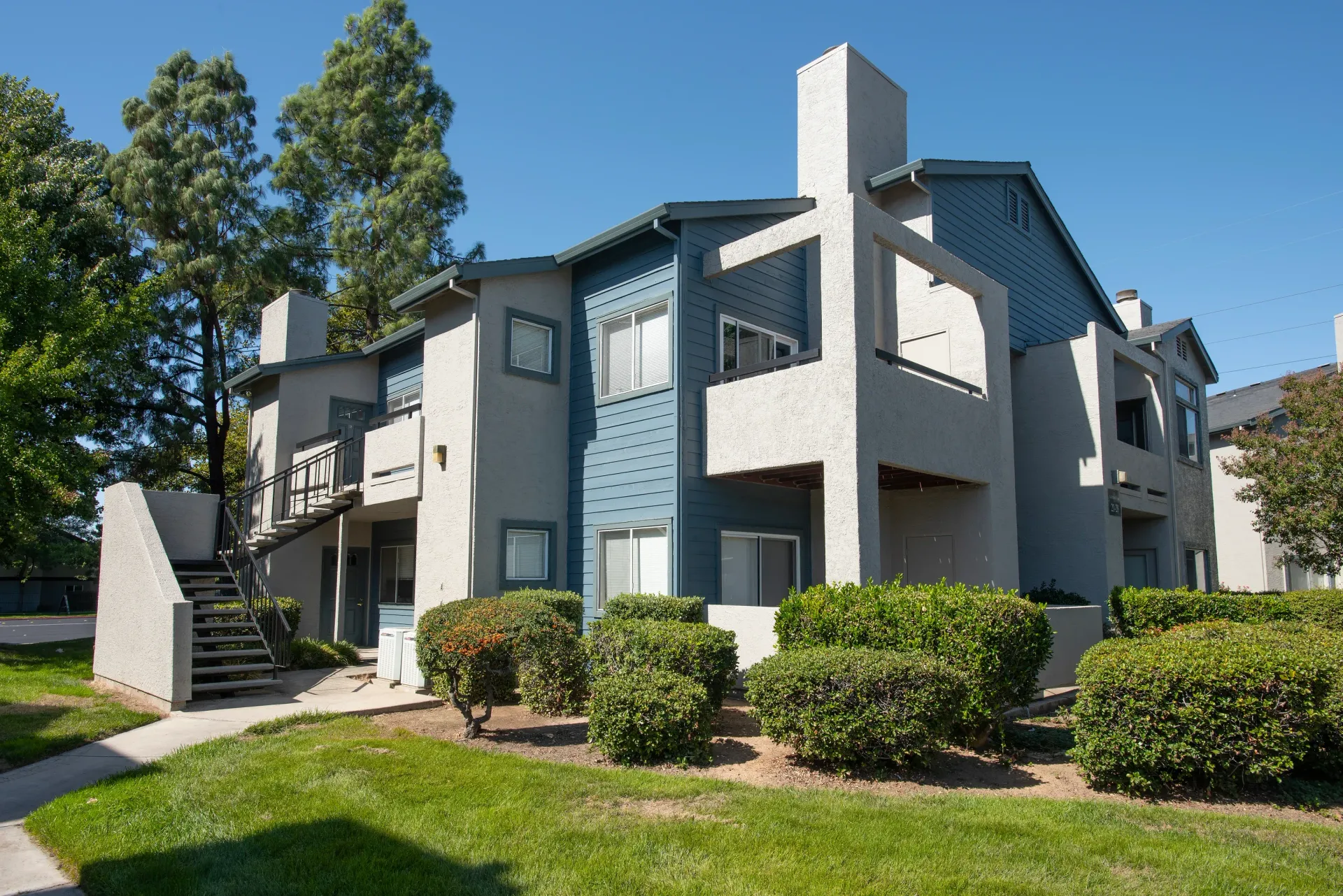 Exterior view of a modern apartment complex with staircases and landscaped shrubs.