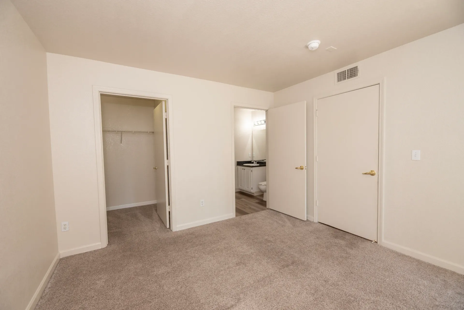 Neutral bedroom with beige walls, carpet, a closet, and two doors.