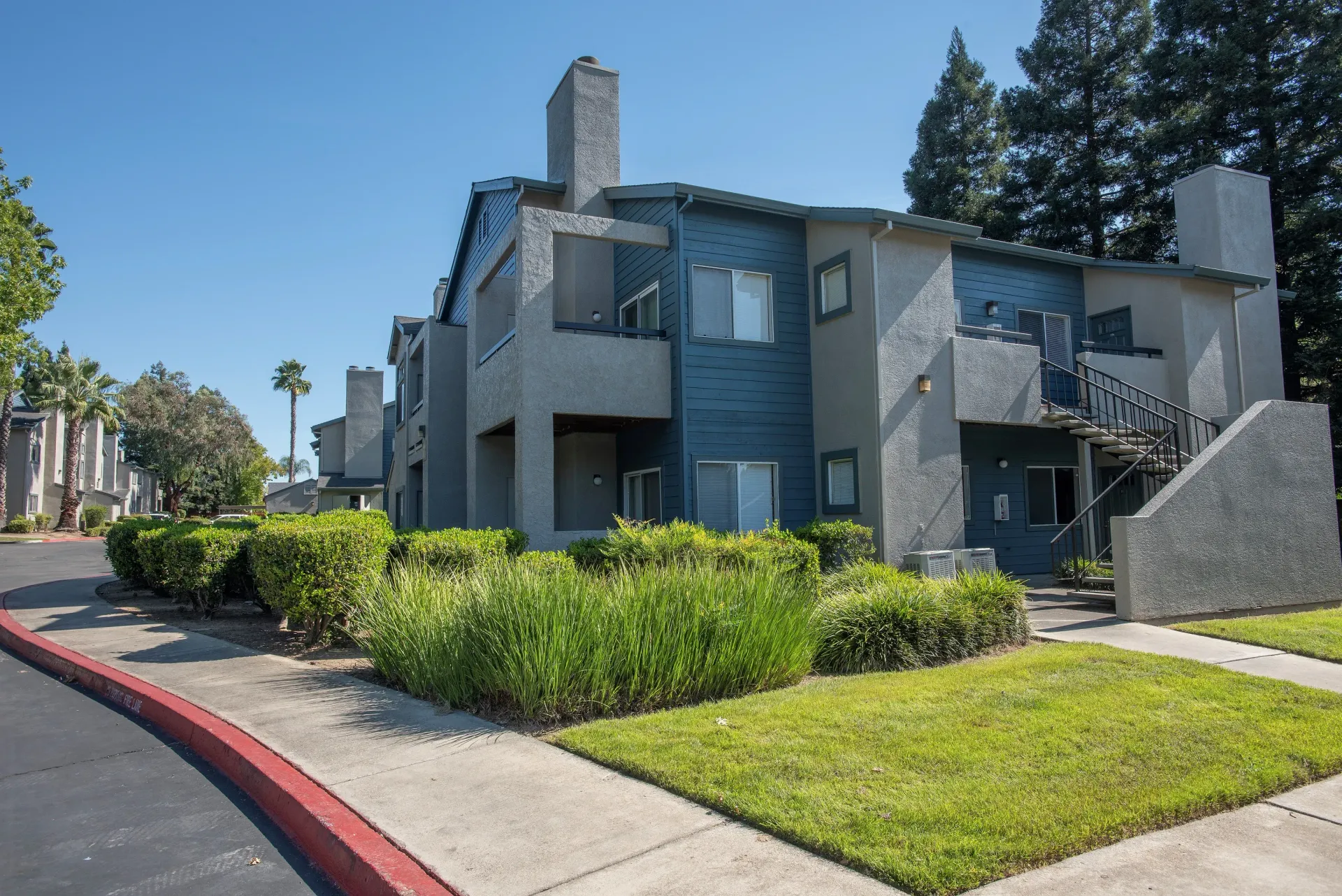 Exterior view of a modern apartment building with blue siding, stairs, and landscaping.
