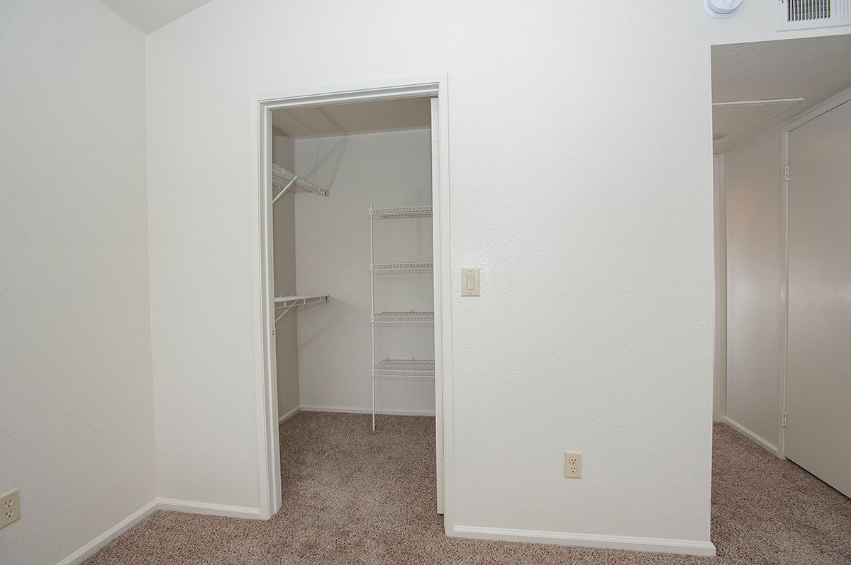 Open walk-in closet with wire shelves and a hanging rod in a neutral-toned apartment.