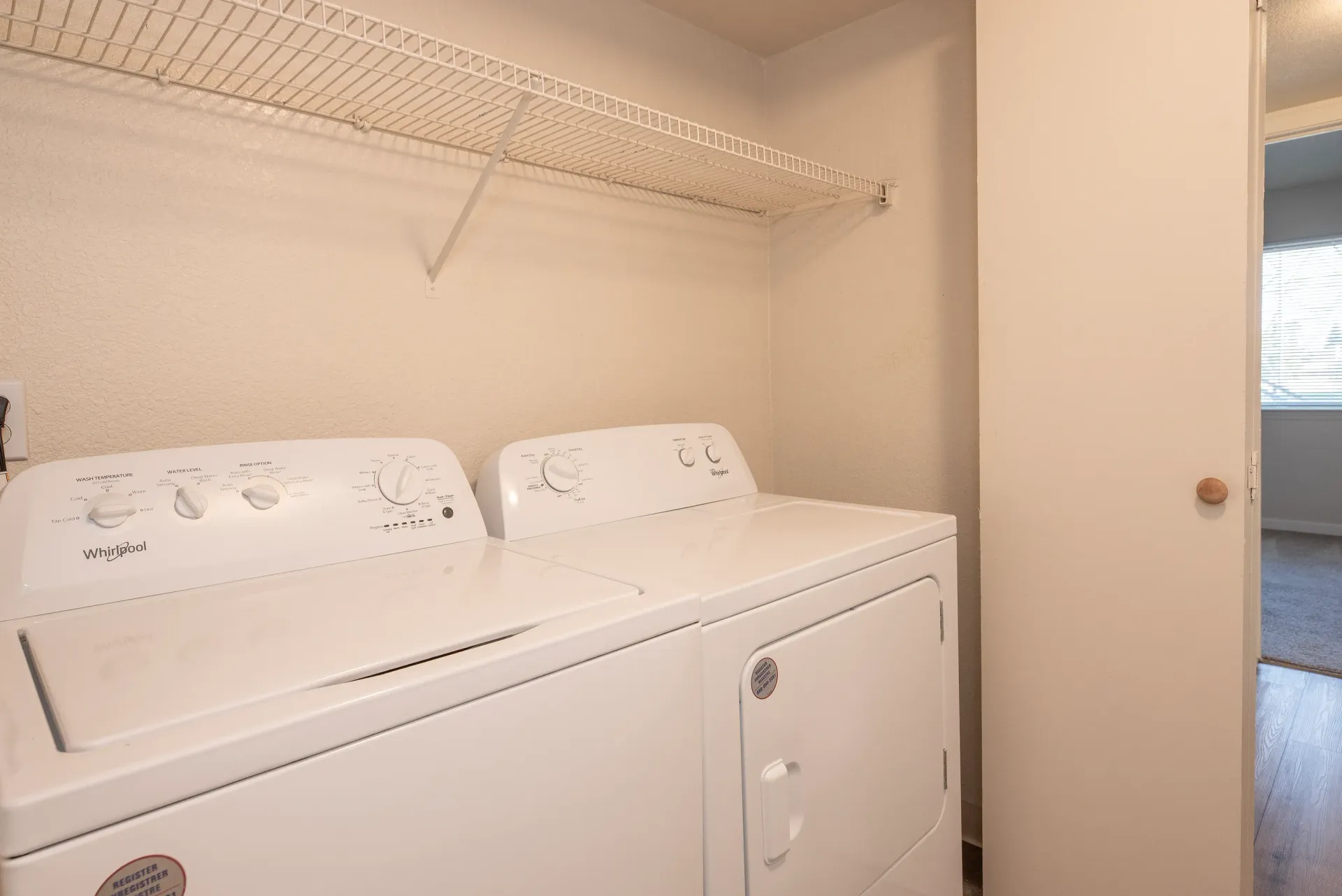 Laundry closet with white washer and dryer side by side beneath a wire shelf.