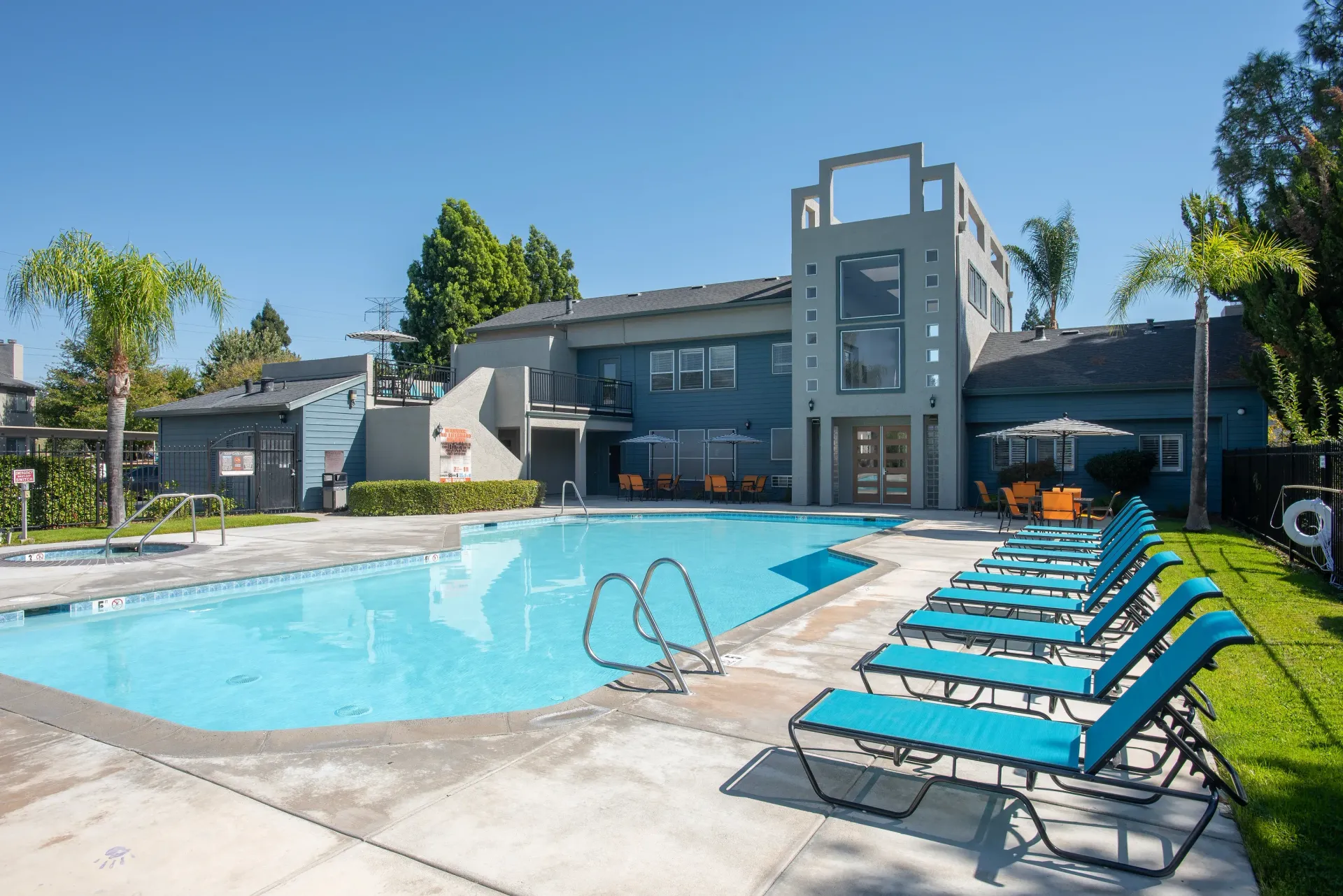 Outdoor apartment community pool with blue water, lounge chairs, and surrounding building.