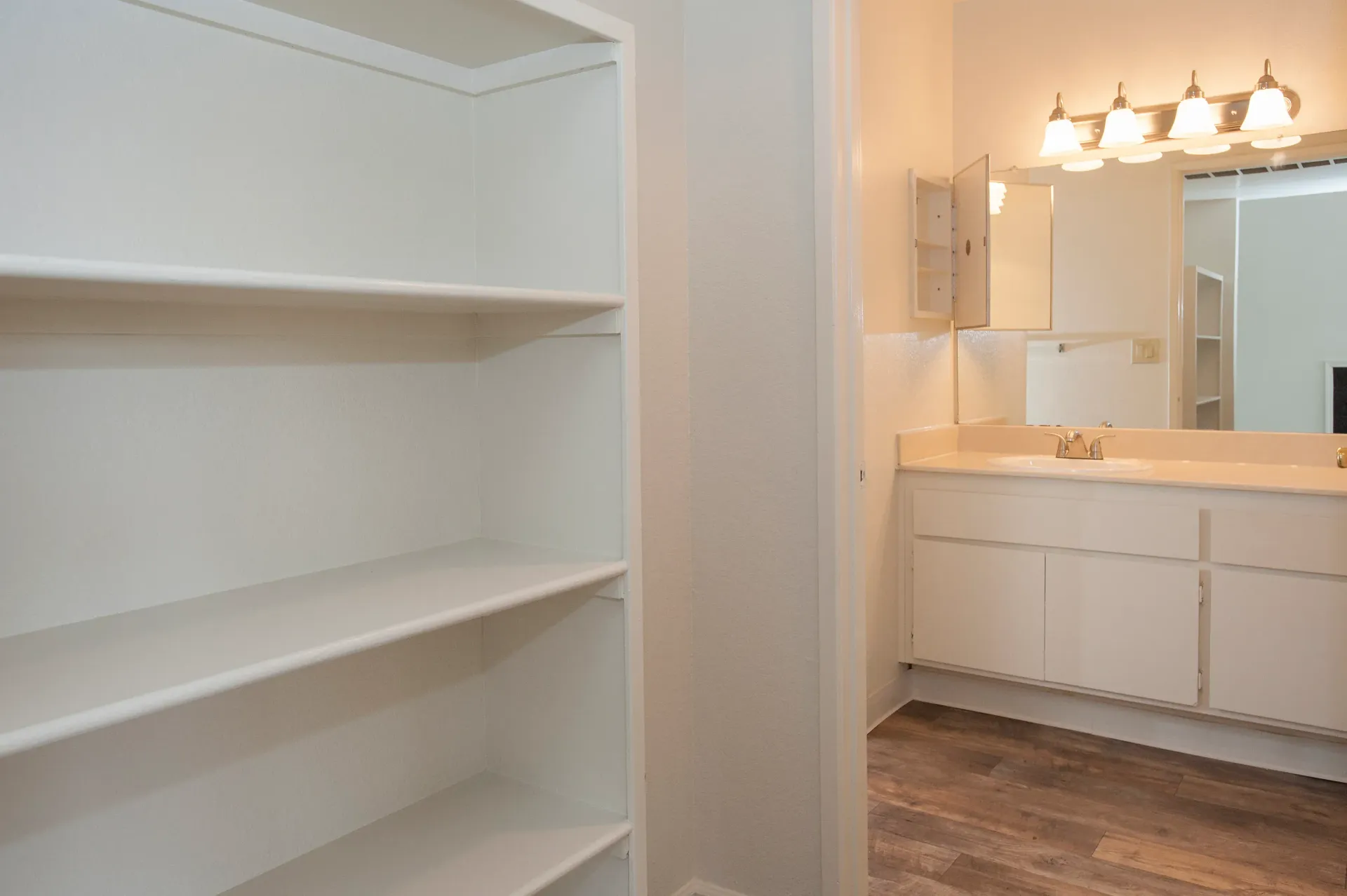 Bright white bathroom with single-sink vanity, mirrored cabinet, and open shelves on the left.