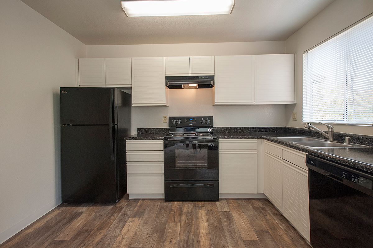 Kitchen with white shaker cabinets, black appliances, and a double sink under a window.
