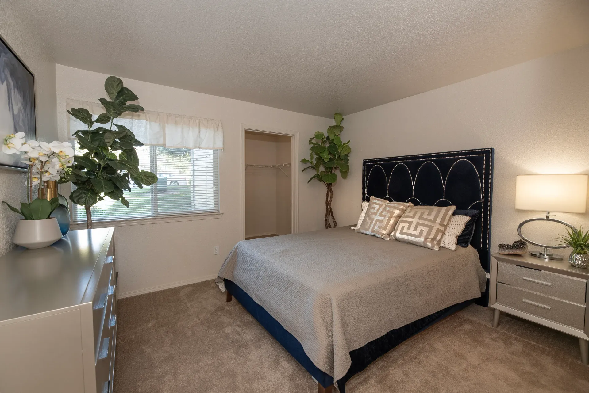Bedroom with a queen bed, two nightstands, dresser, plants, and a window.
