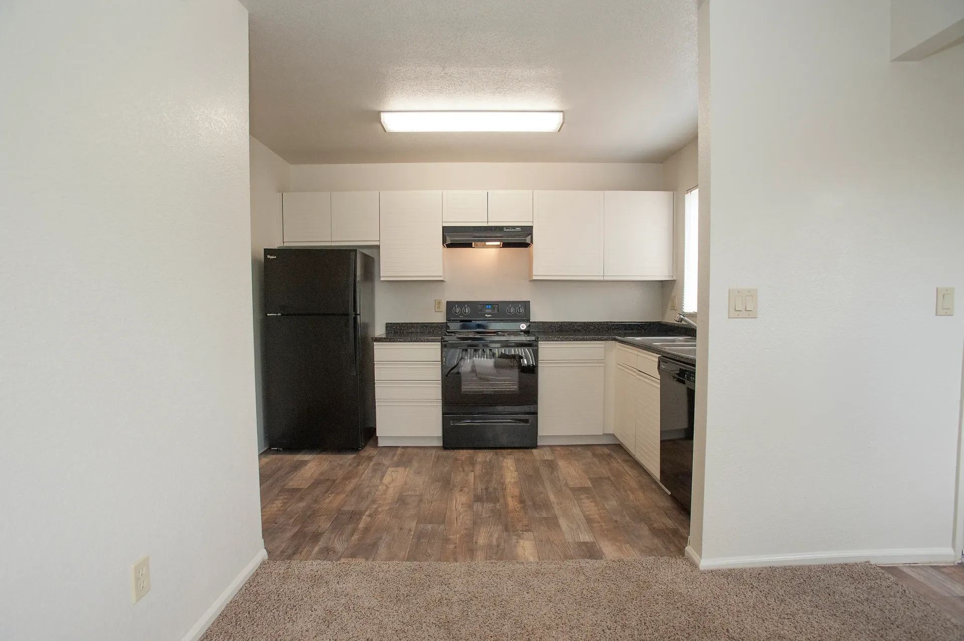 Kitchen in an apartment with white cabinets, black appliances, and wood-look flooring.