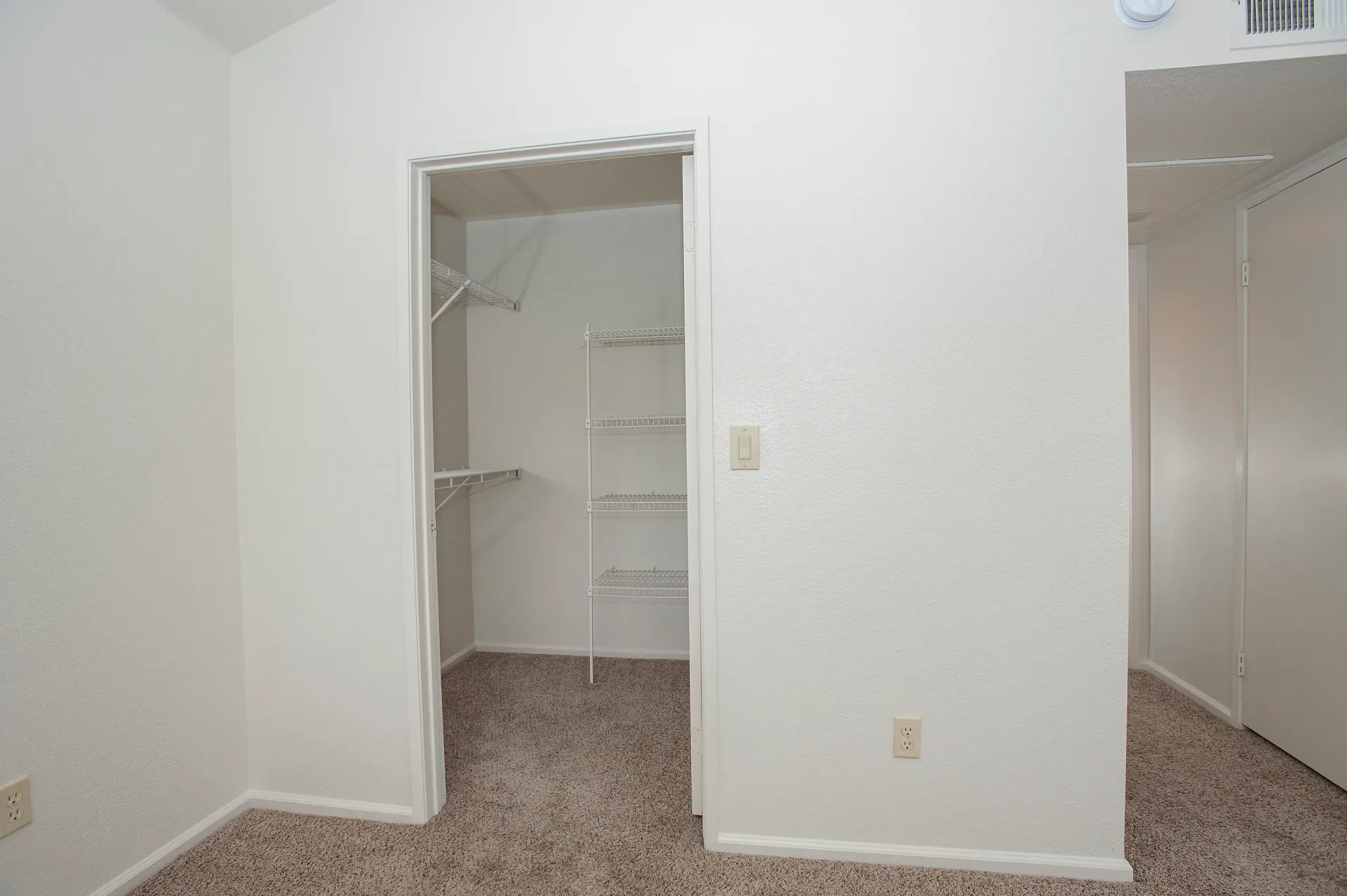 Open walk-in closet with wire shelving and hanging rod in carpeted room.