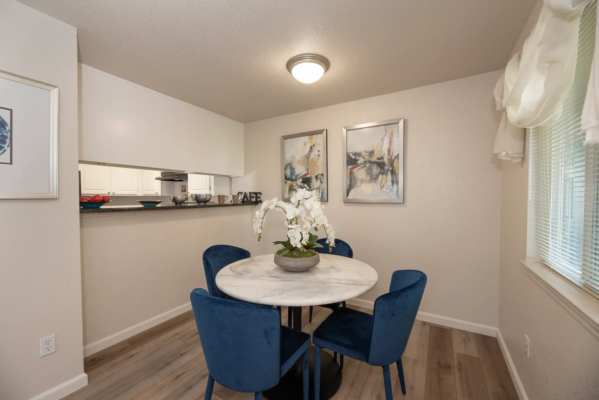 Dining area in an apartment with a round marble table, blue chairs, and a pass-through to the kitchen.