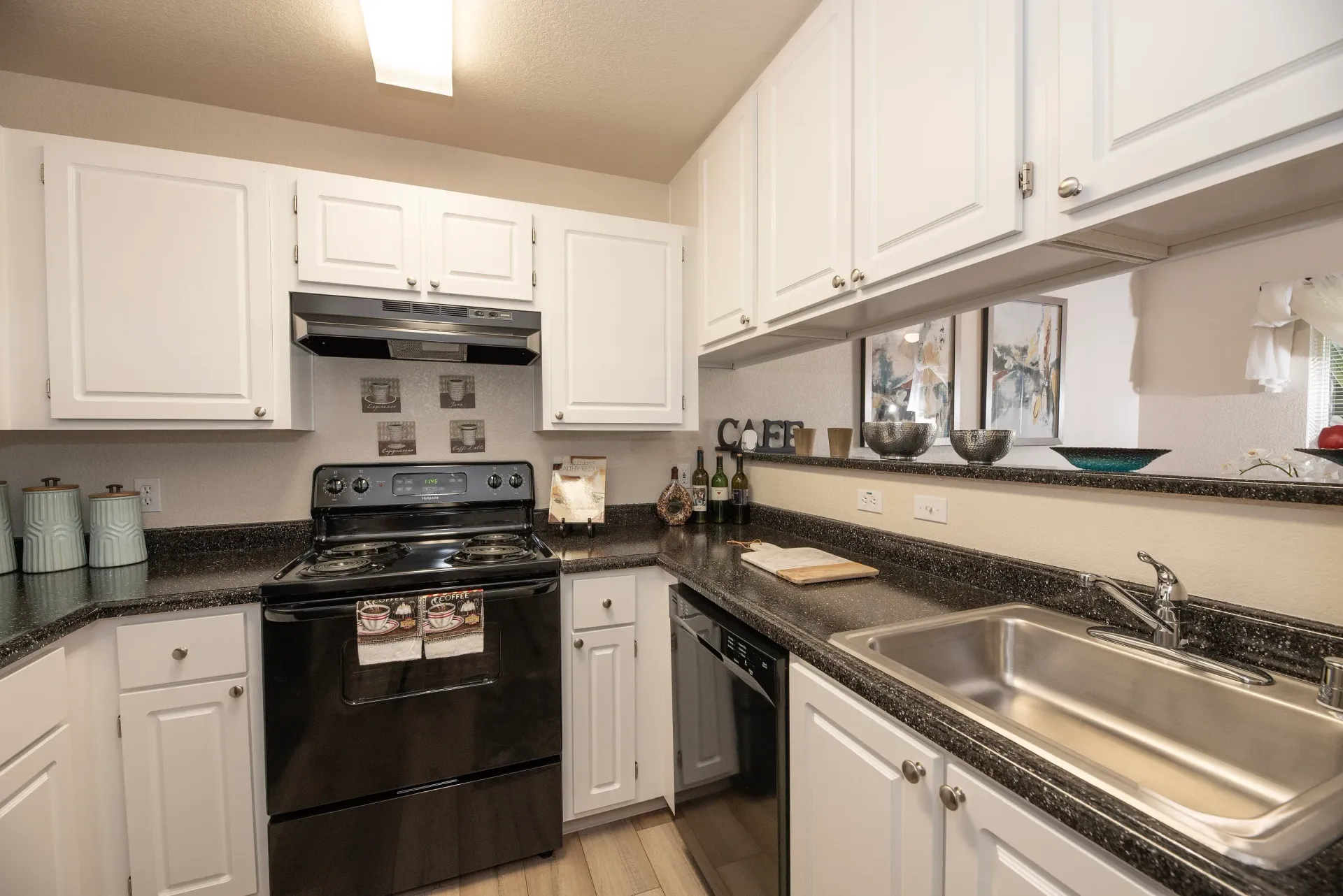 Compact apartment kitchen with white cabinets, black speckled countertops, a stove, and a stainless steel sink.