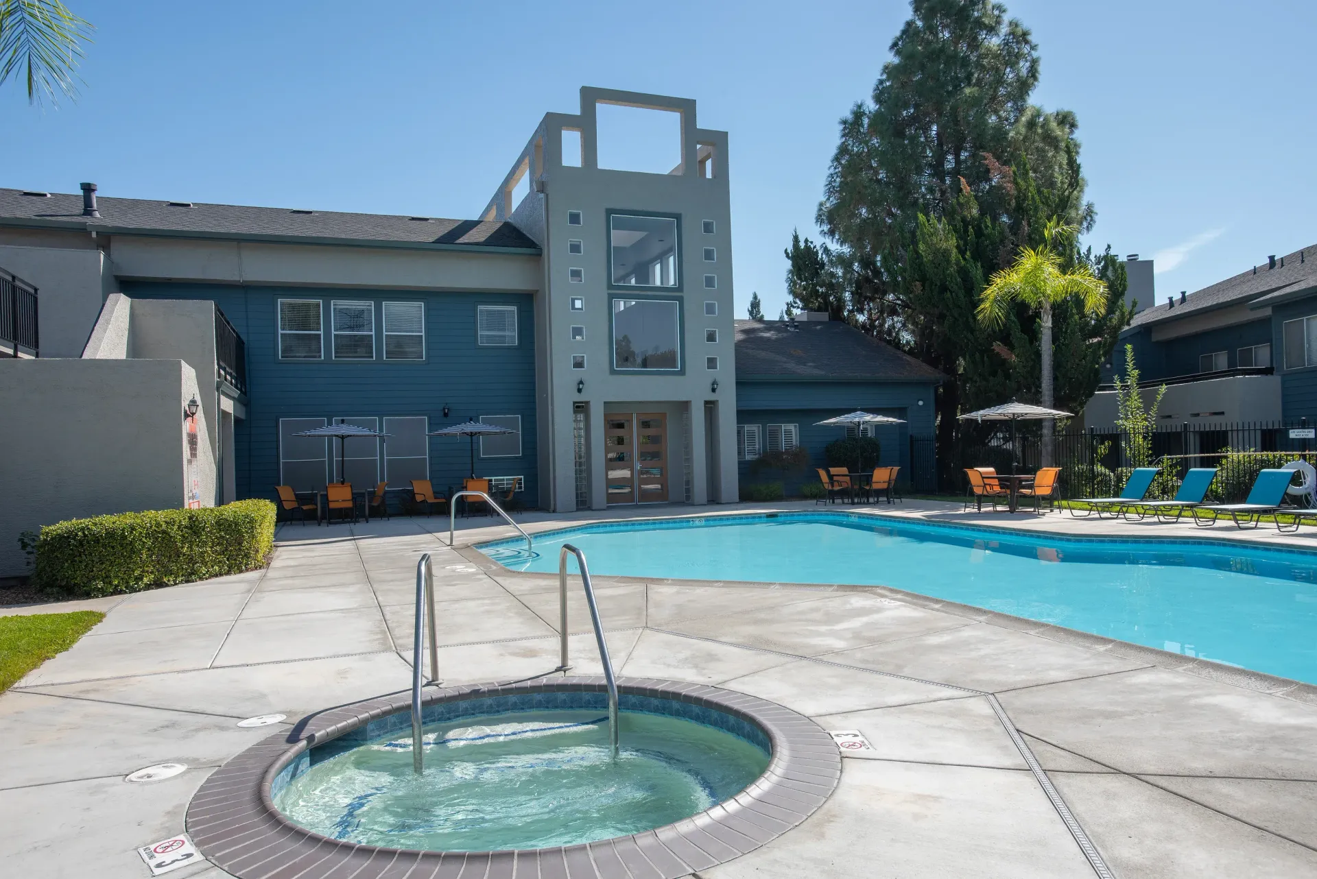 Outdoor apartment community pool with a hot tub and lounge chairs.