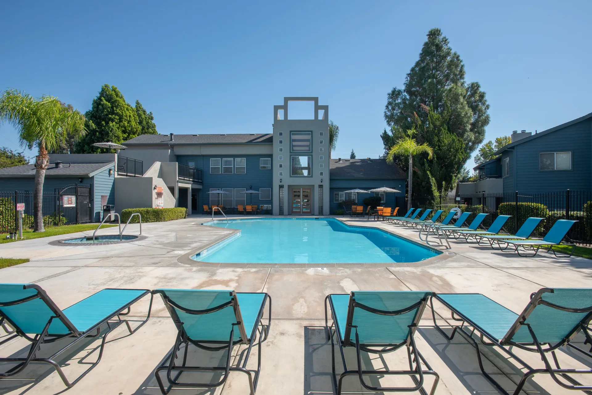 Outdoor apartment community pool with blue water, lounge chairs, and umbrellas.