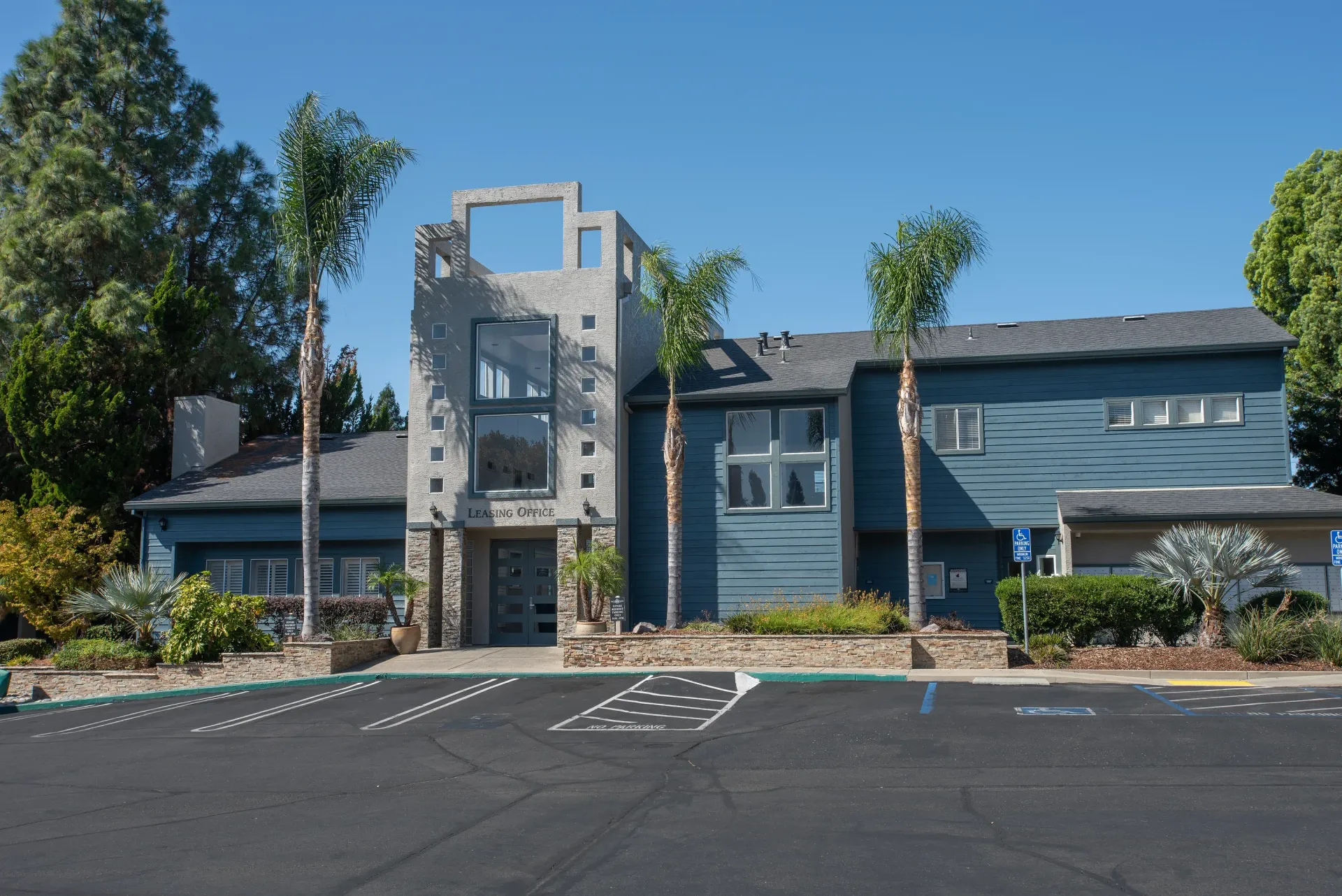 Exterior view of a modern apartment leasing office with blue siding and palm trees.